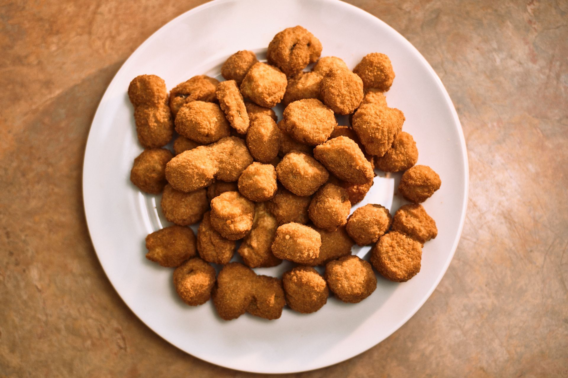 A white plate topped with fried chicken nuggets on a table.