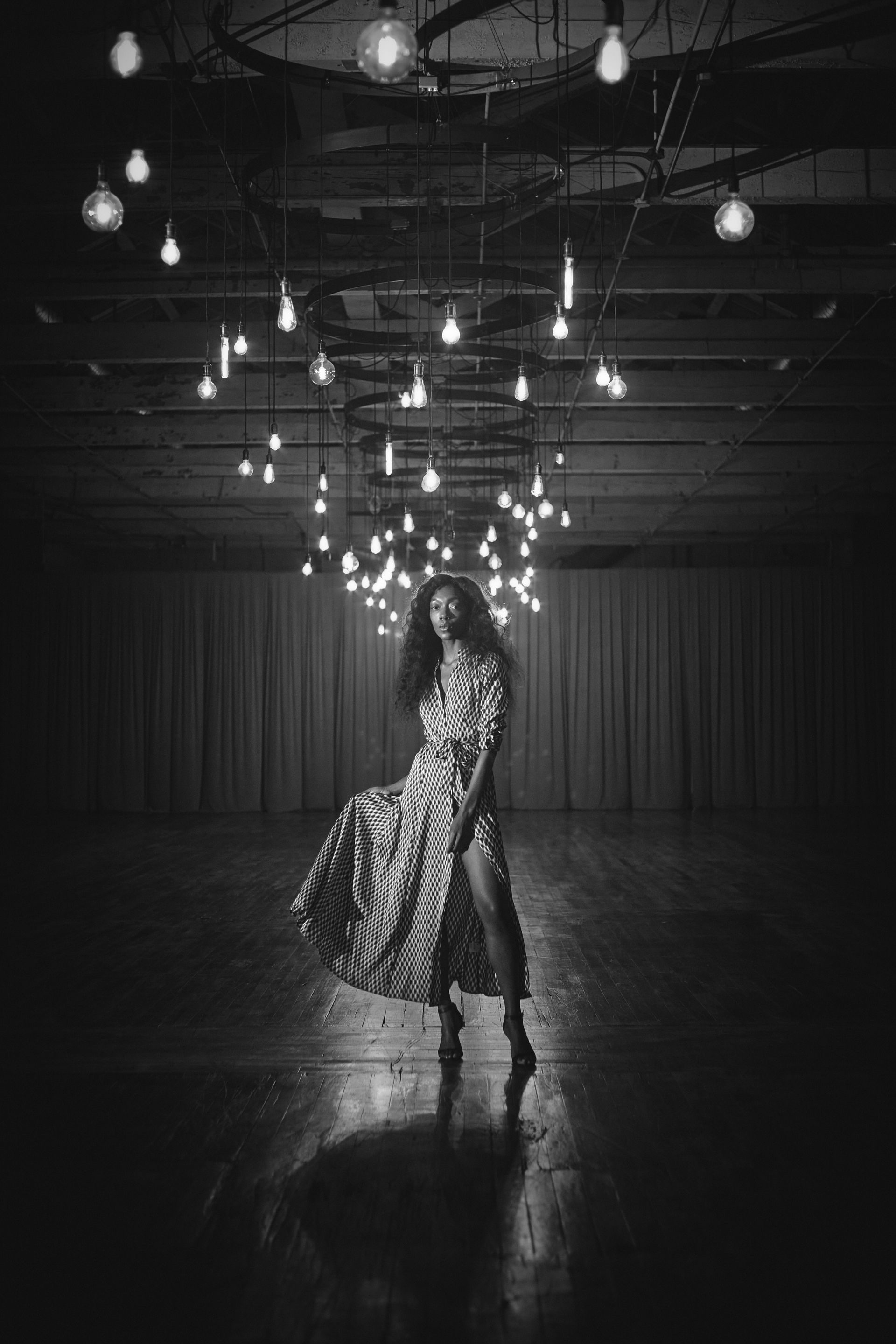 Woman in white dress and scarf on a rock by the sea, holding scarf above her head in sunlight.