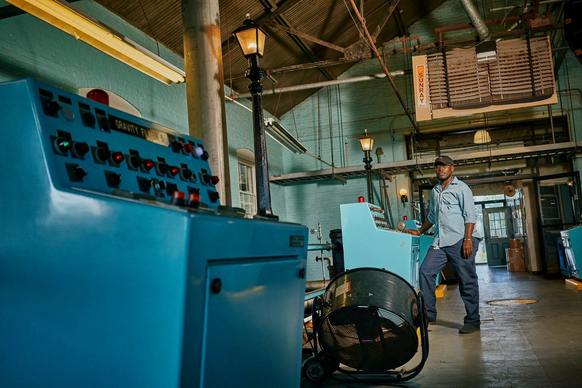 Man in blue shirt stands near a control panel in an industrial setting.