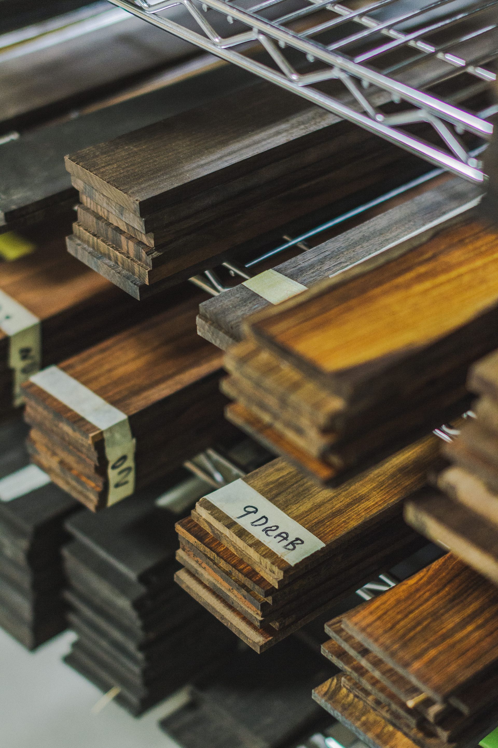 Stacks of various wood strips on a shelf, labeled and showing different shades of brown.
