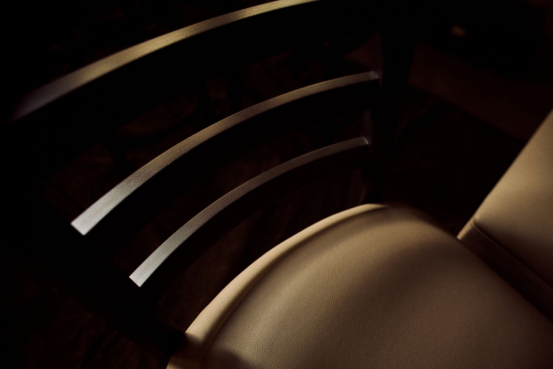 Close-up of a tan chair with curved back, featuring dark shadows and reflective horizontal slats.