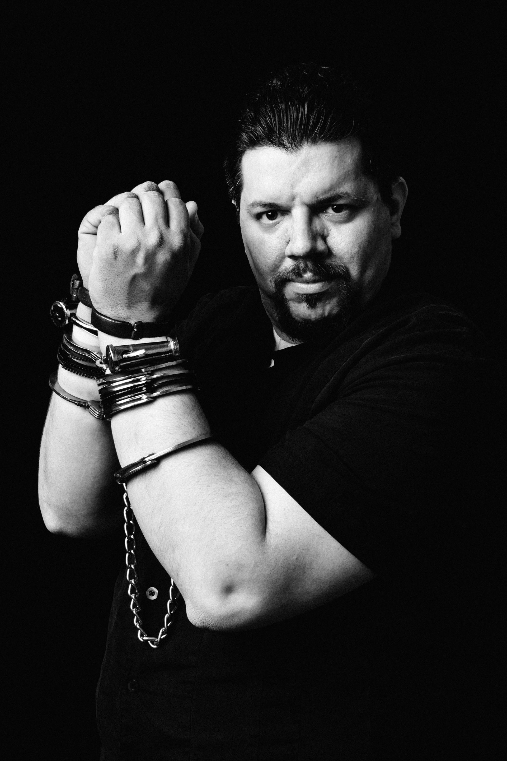 A man with a beard is wearing bracelets on his wrists in a black and white photo.