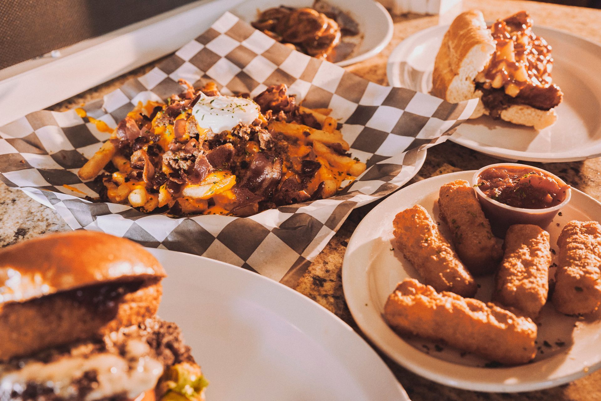 Close-up of various dishes: fries, hot dogs, burger, and fried cheese sticks, on a table.