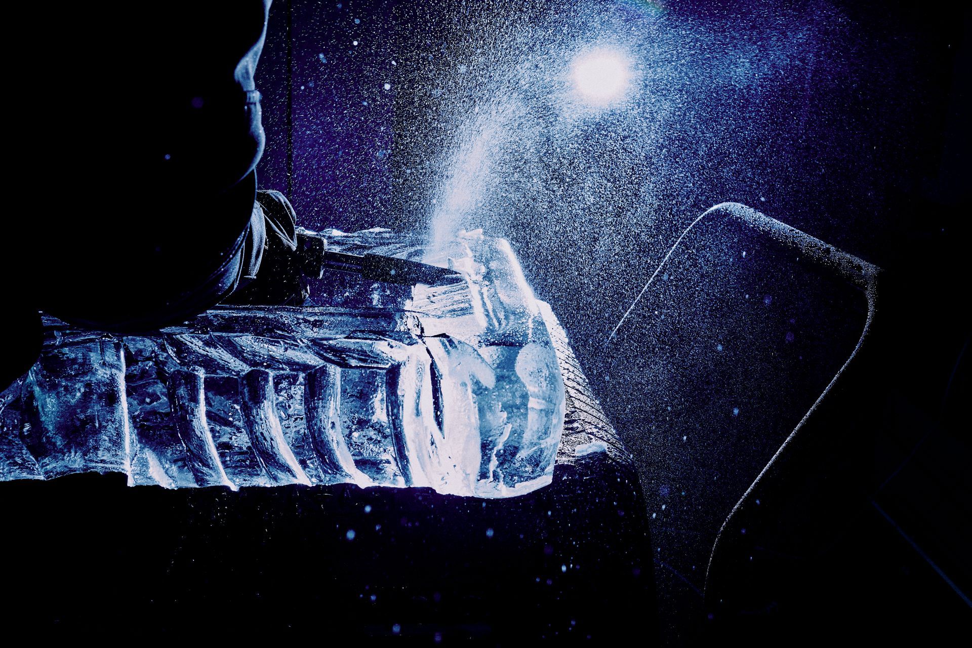 Person shattering a block of ice with a hammer in a dark, blue-lit setting.