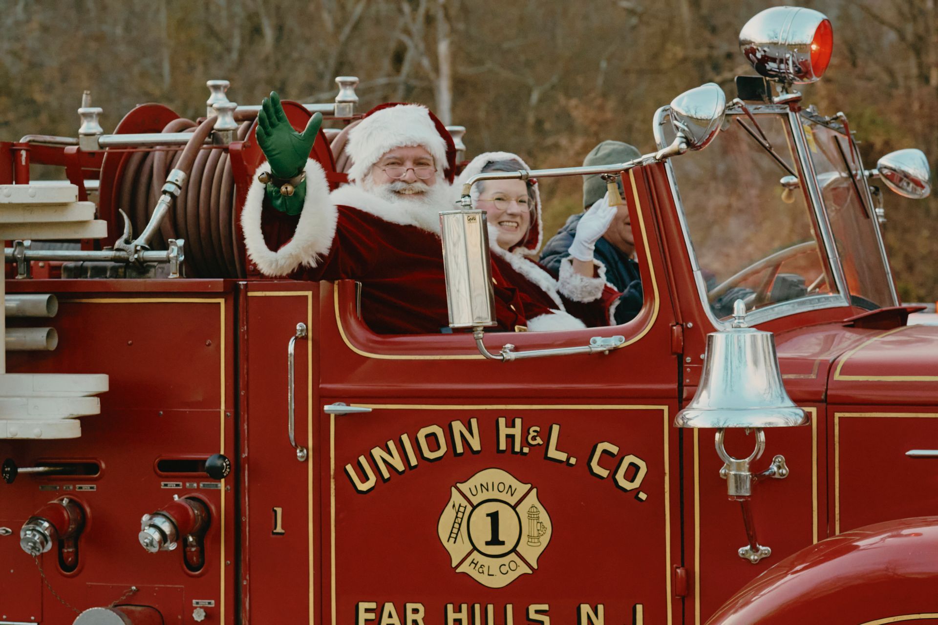 Santa waving from a red fire truck, with a woman,