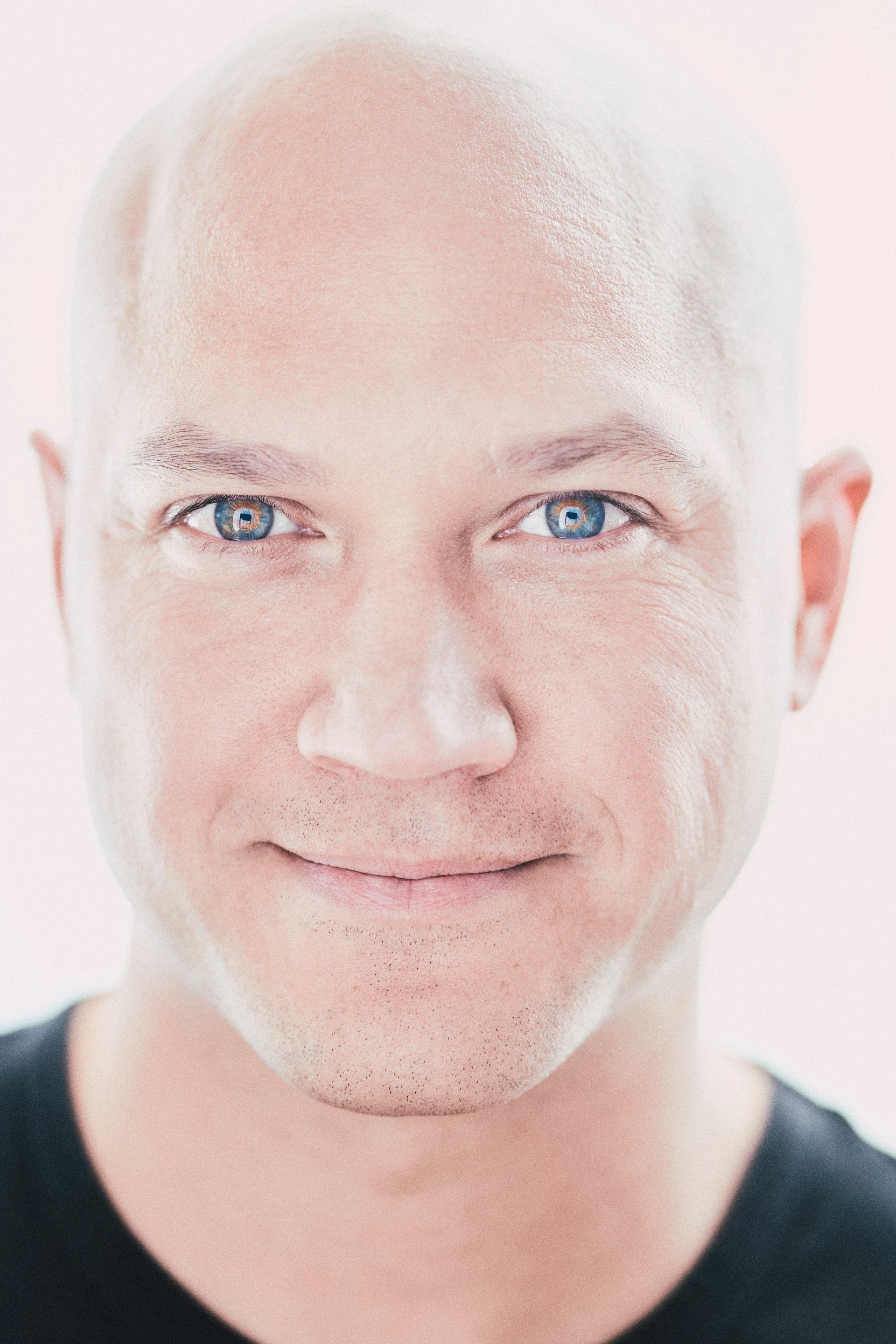 Bald man with blue eyes smiles, looking directly at the camera.