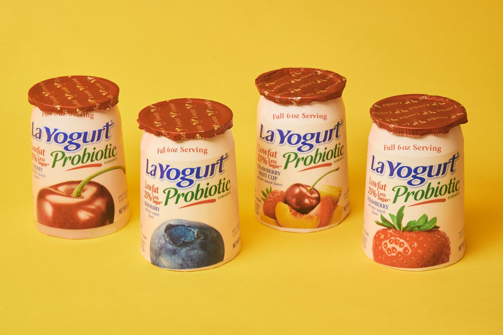 Four La Yogurt probiotic containers, various fruit flavors, against a yellow background.