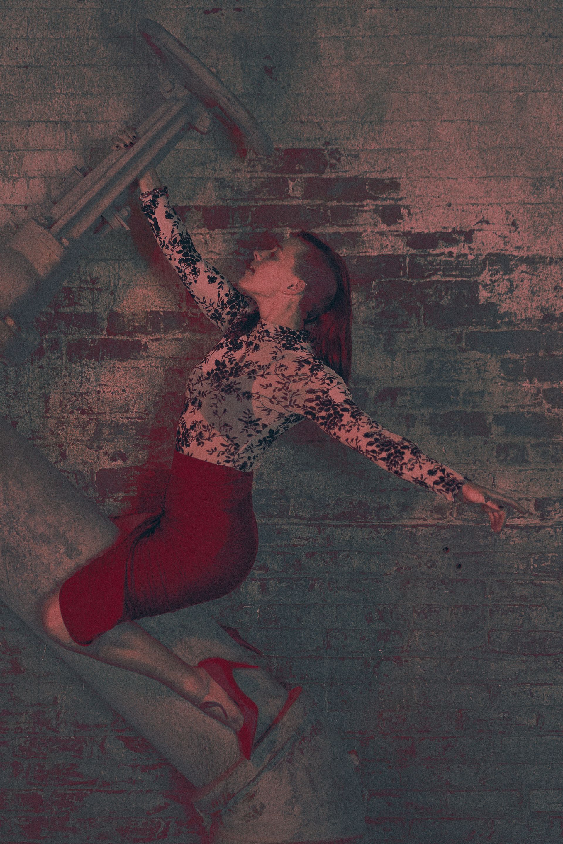 Woman in red skirt and heels, arms outstretched, against a brick wall with architectural elements.