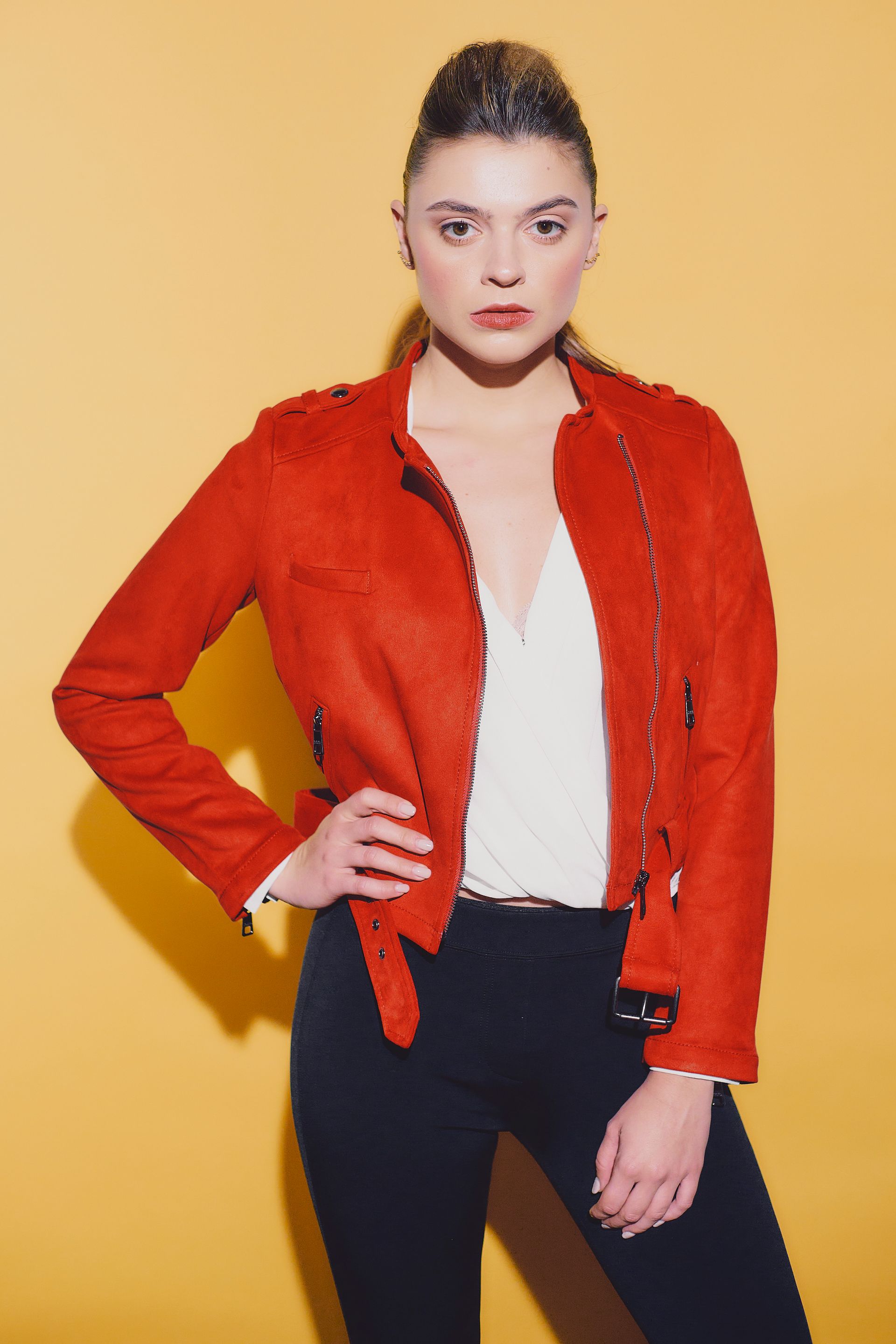 Woman in red jacket and black pants poses in front of a yellow background.