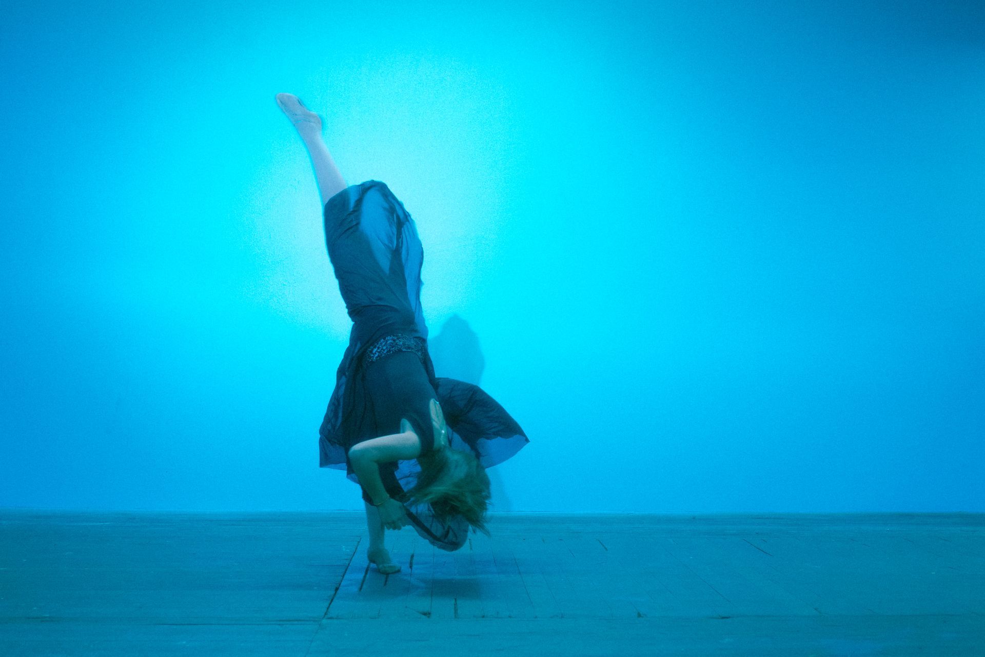 A woman is doing a handstand in front of a blue wall.