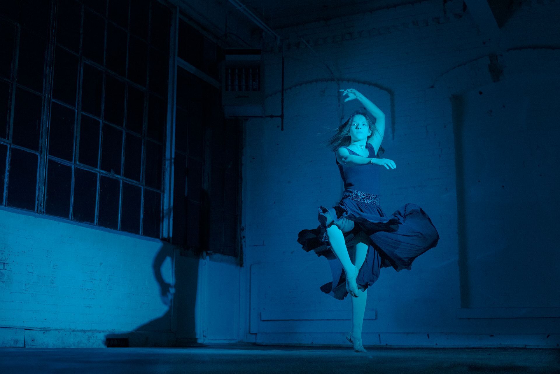 A woman in a blue dress is dancing in a dark room.