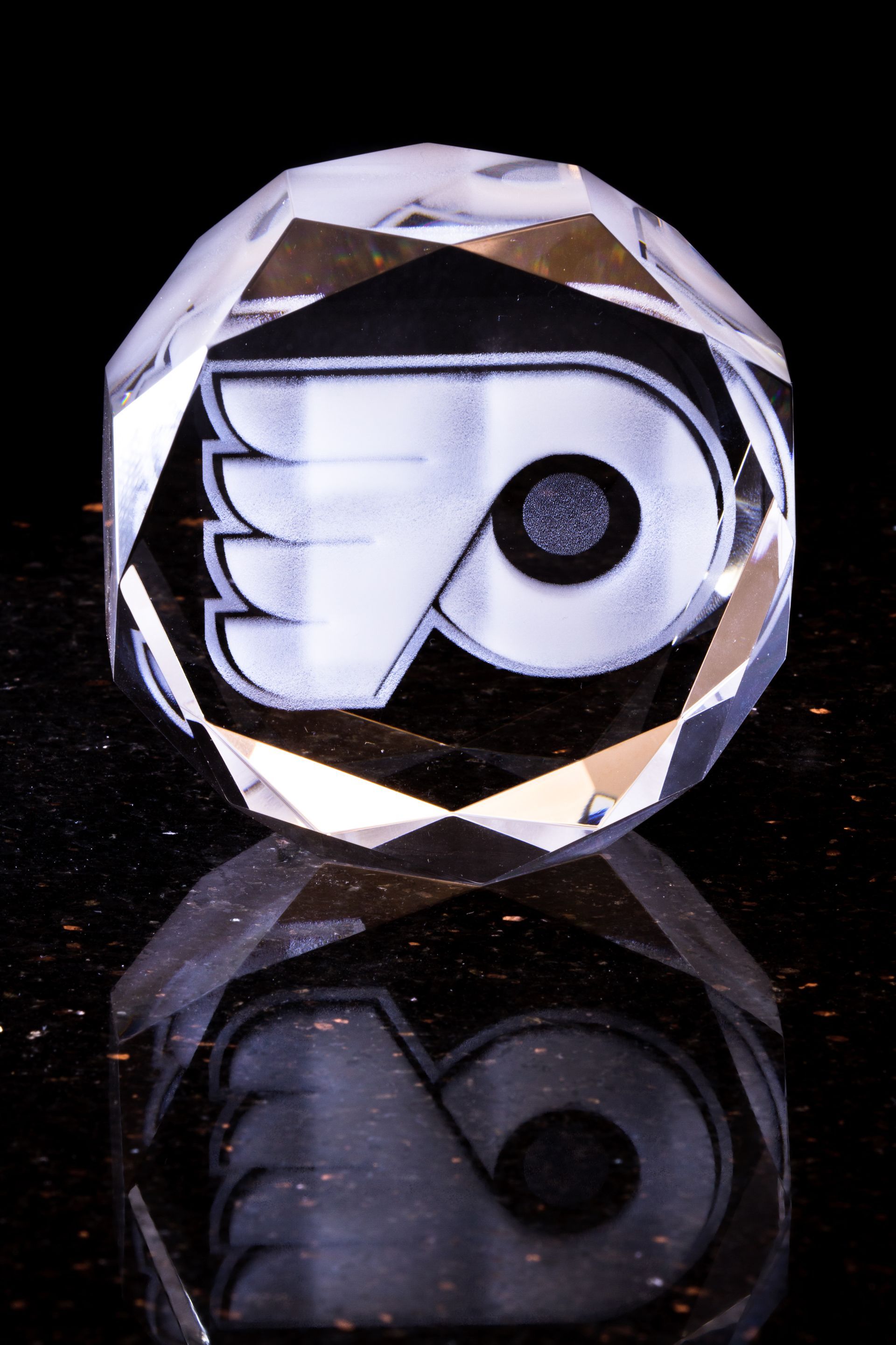 Philadelphia Flyers logo encased in a faceted crystal, reflecting on a black surface.