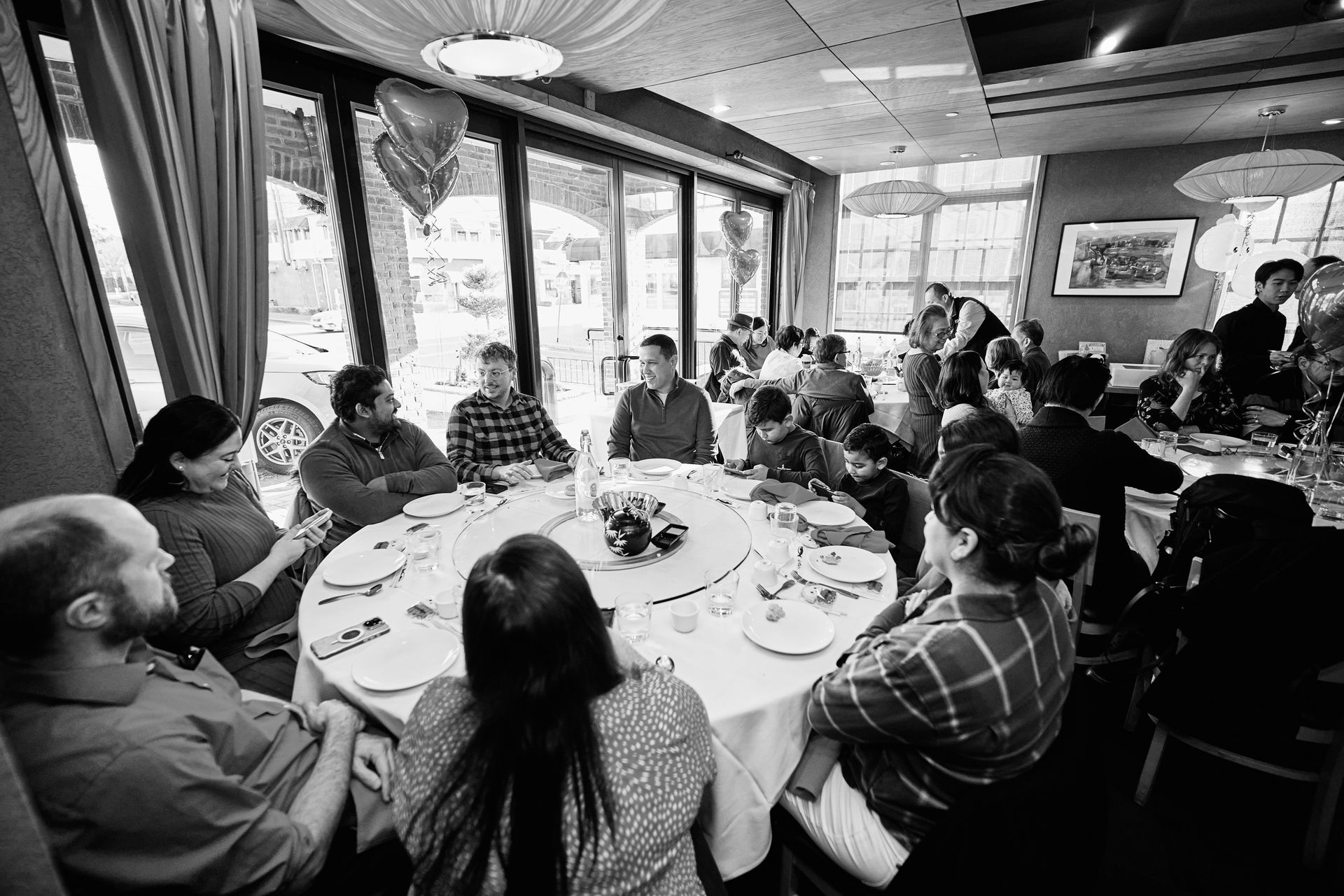 People gathered around a large round table in a restaurant with large windows, eating and talking.