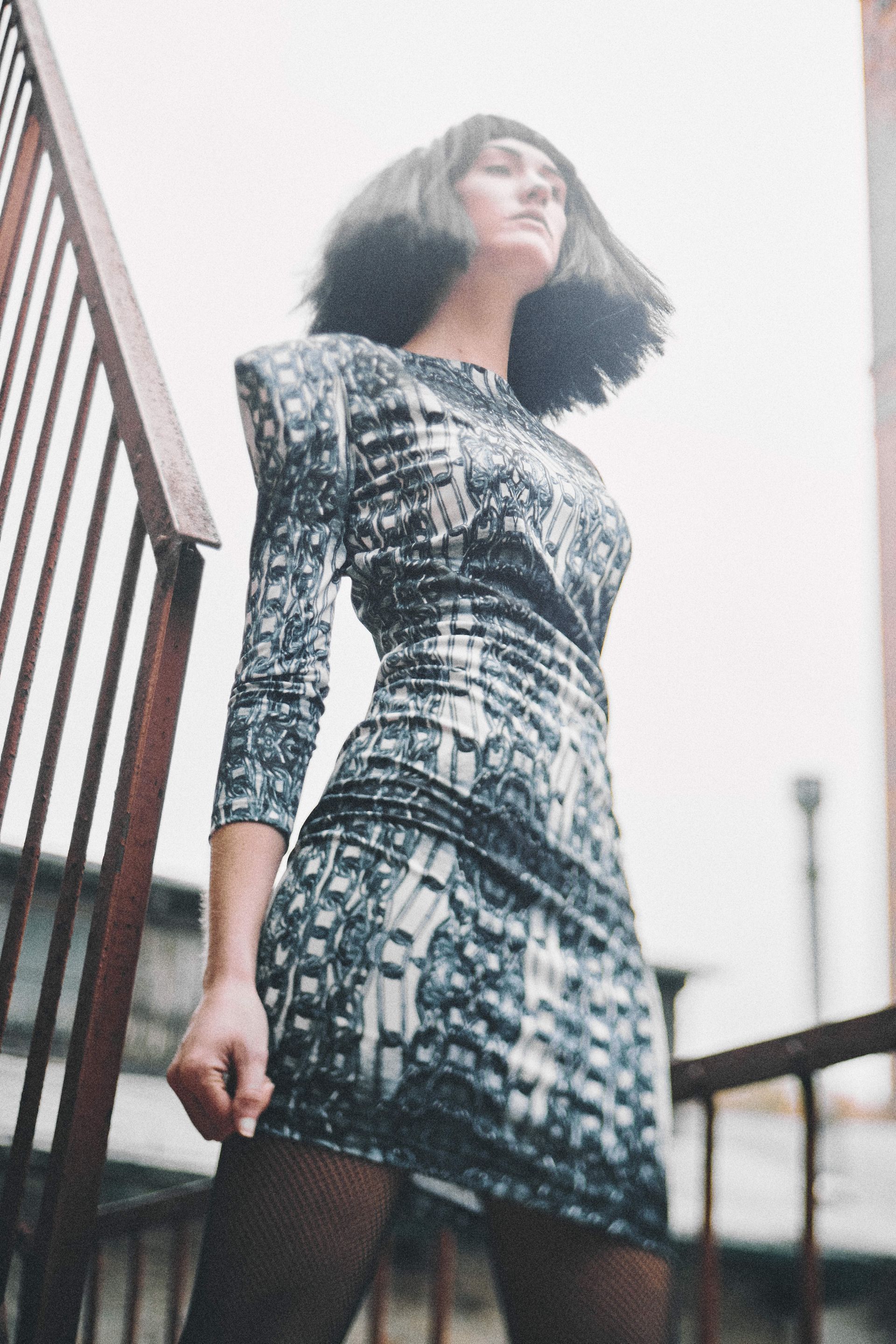 Woman in patterned dress on outdoor stairs, looking up.