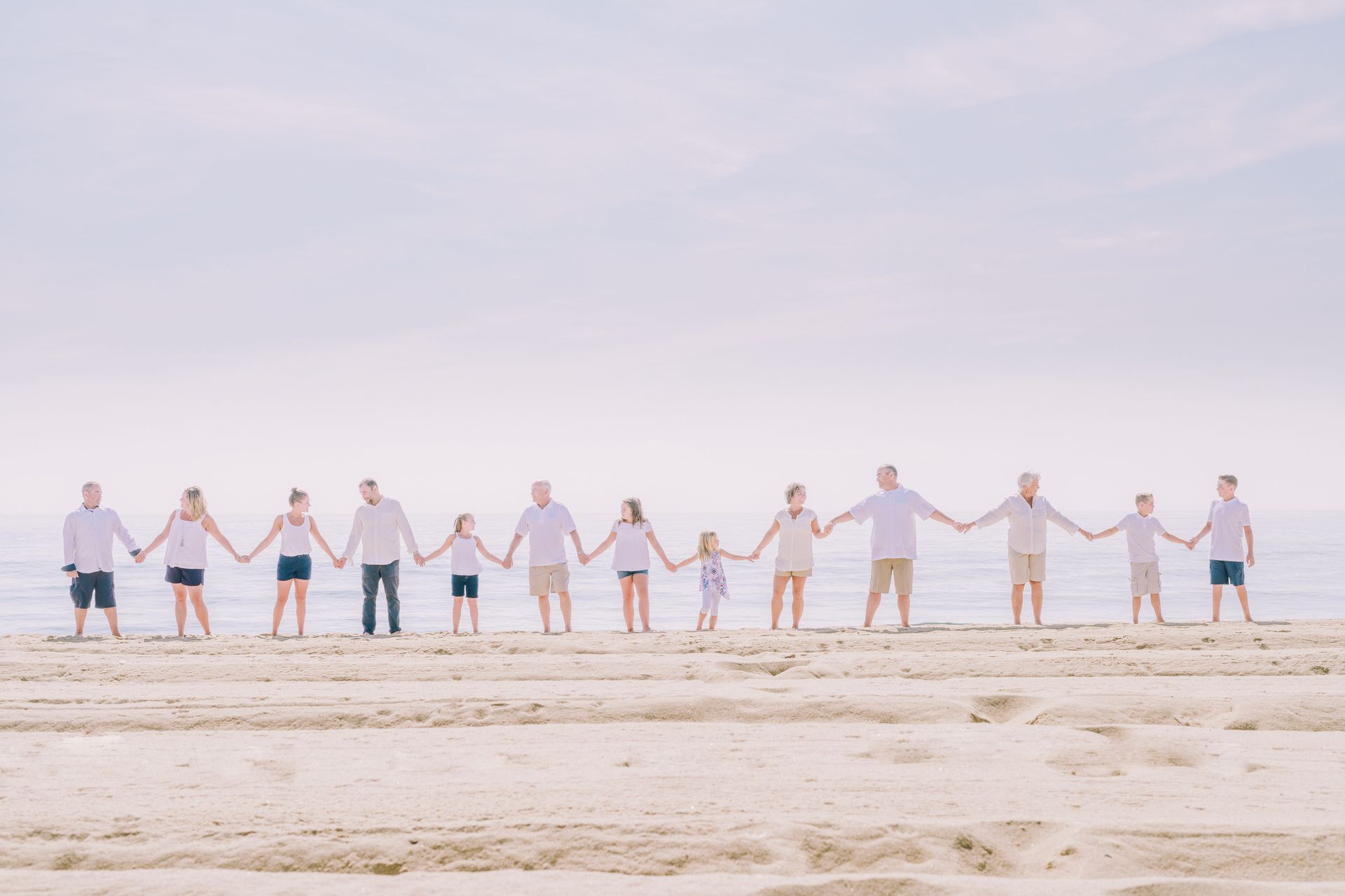 Family holding hands on a beach. White shirts, shorts, and the ocean in the background.