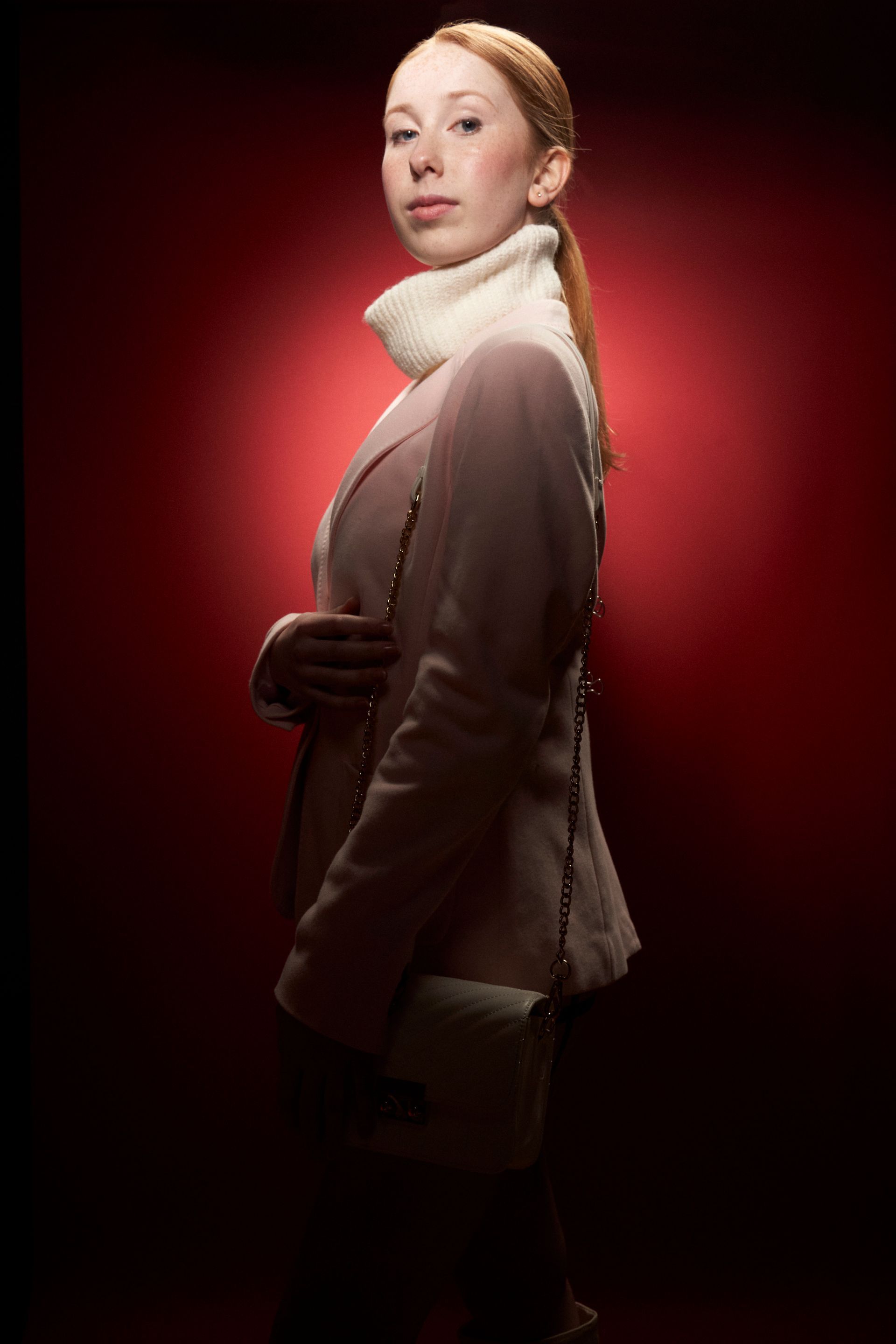 Woman in pink blazer and white turtleneck, red background.