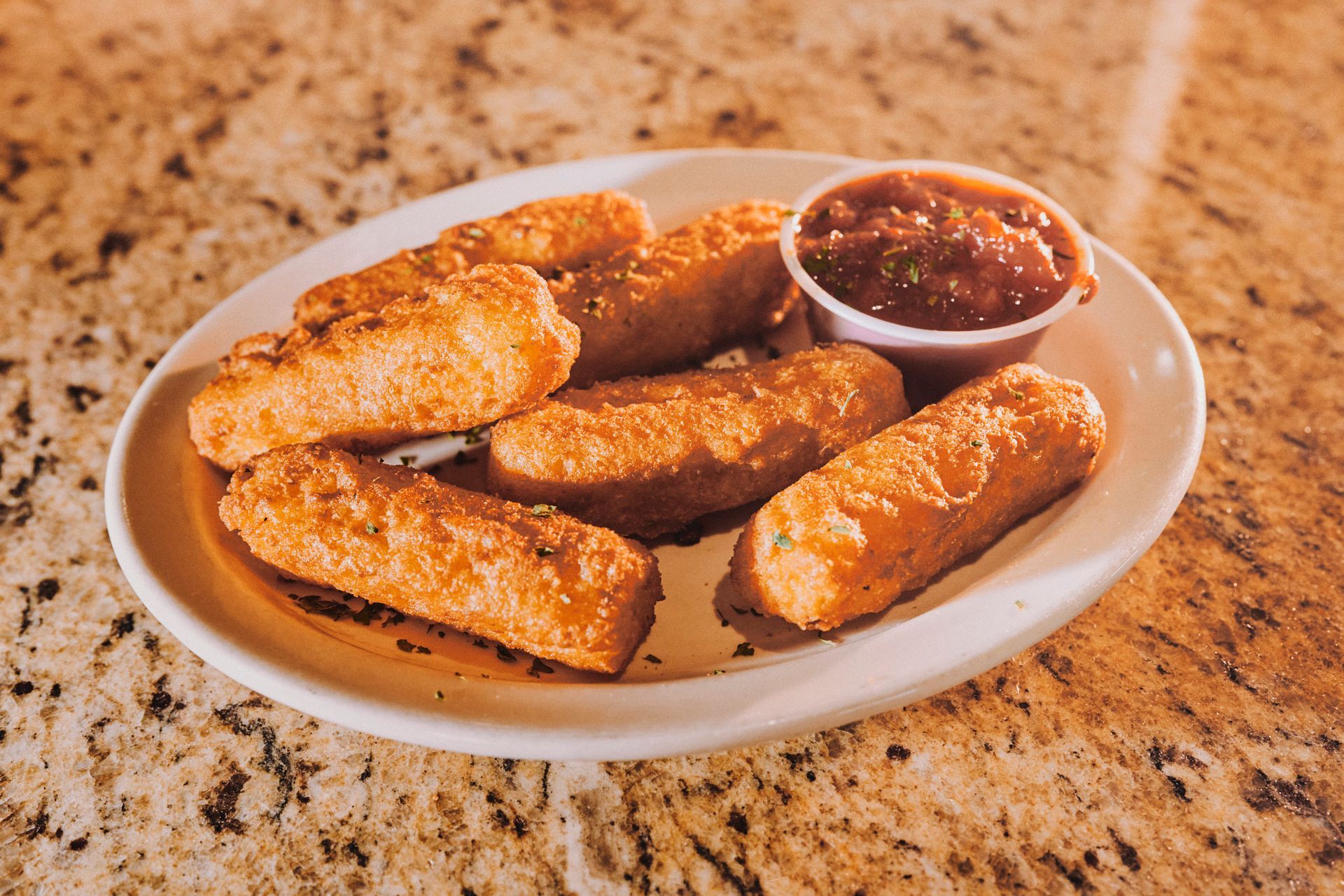 A plate of mozzarella sticks with dipping sauce on a table.