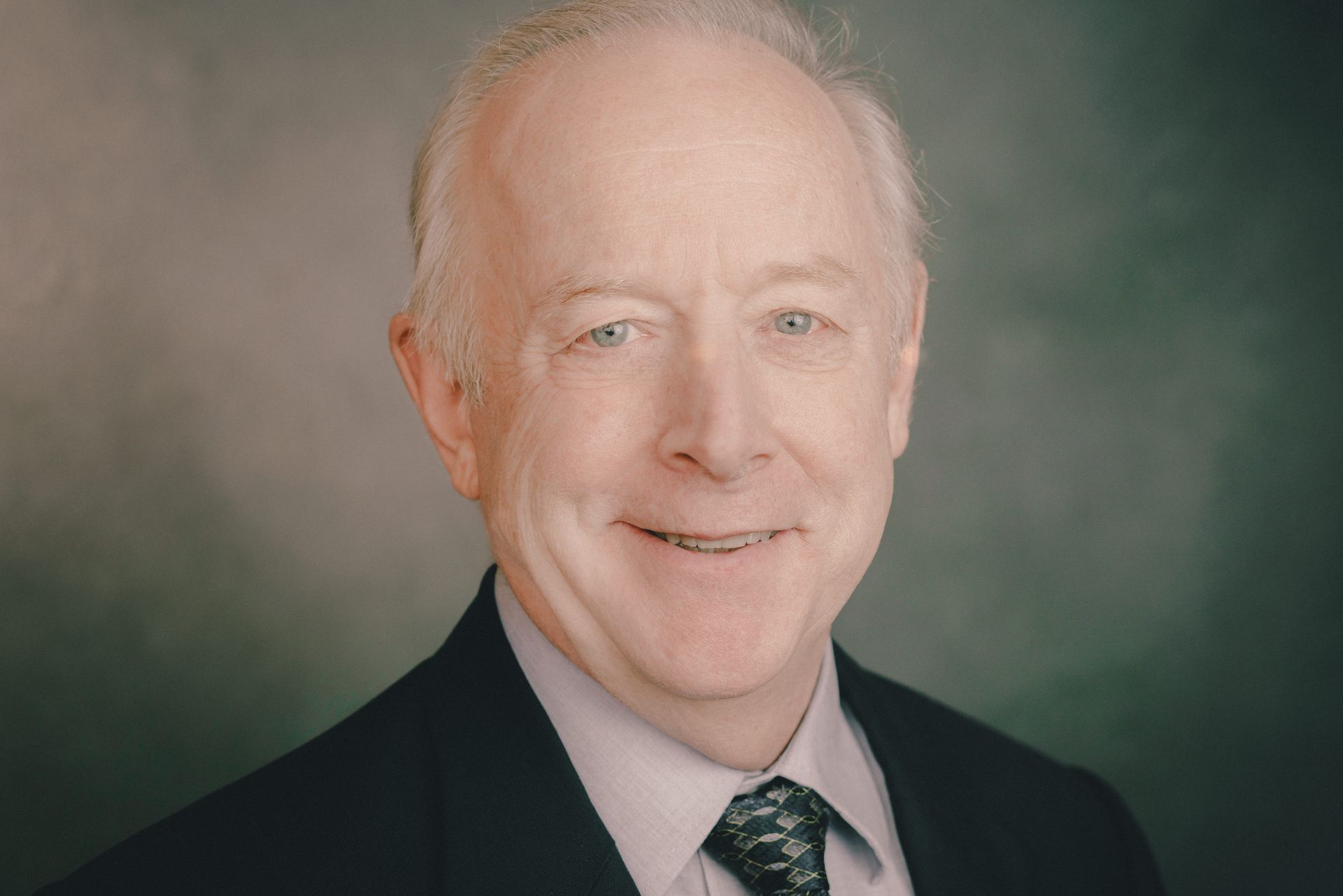 Smiling older white man in a suit and tie, head and shoulders portrait.