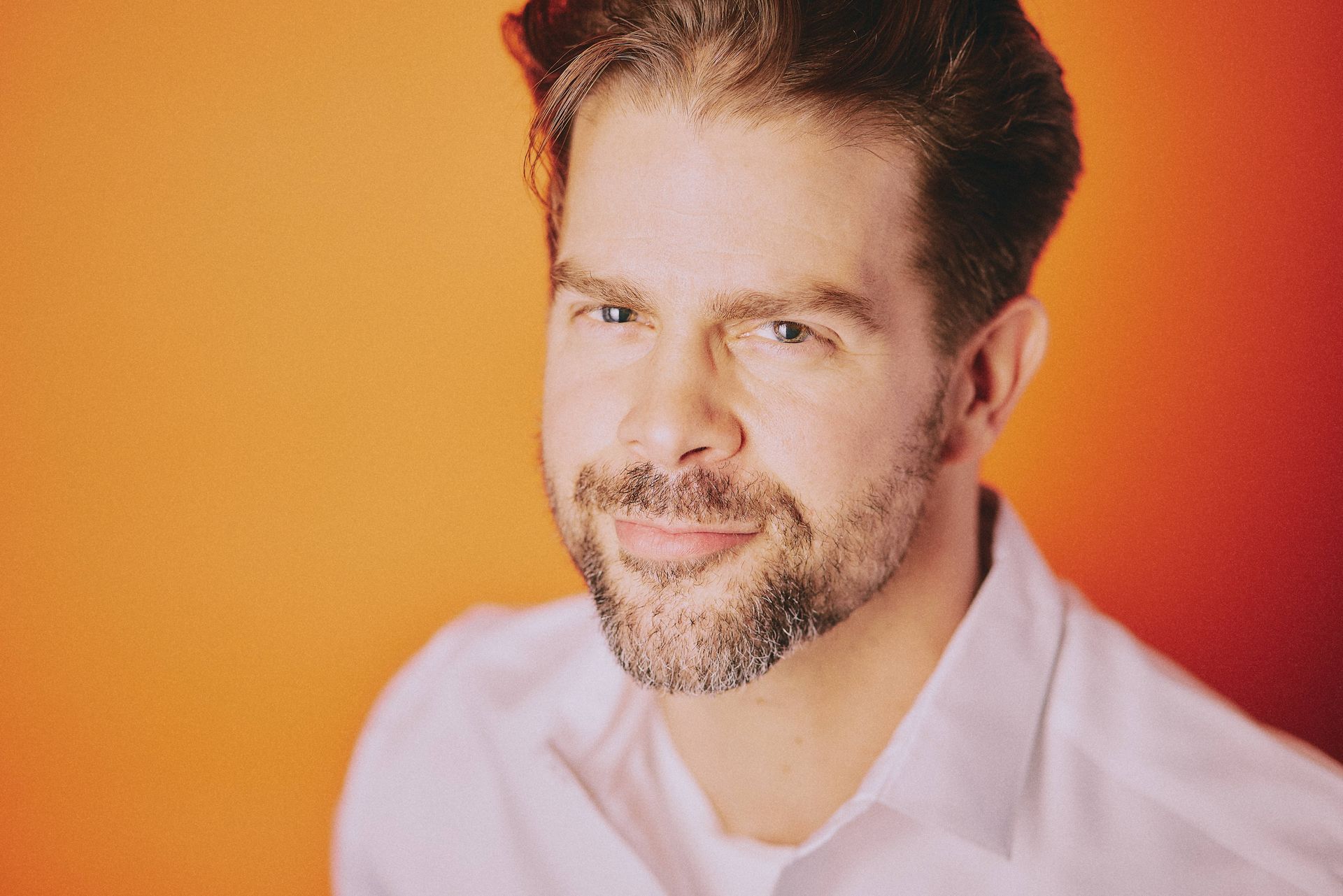 A man with a beard is wearing a white shirt and smiling.