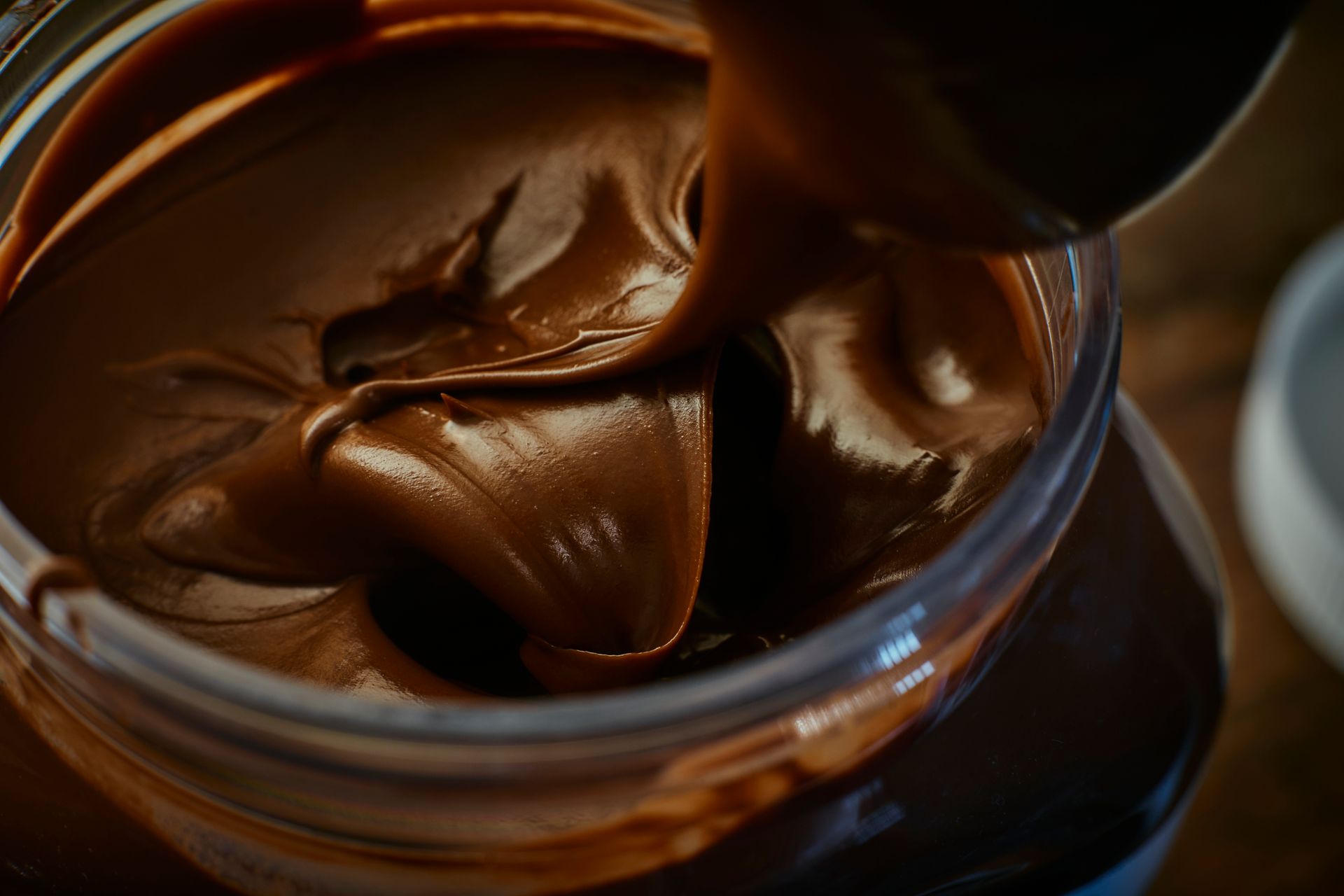 Jar of chocolate hazelnut spread being scooped out with a spoon.