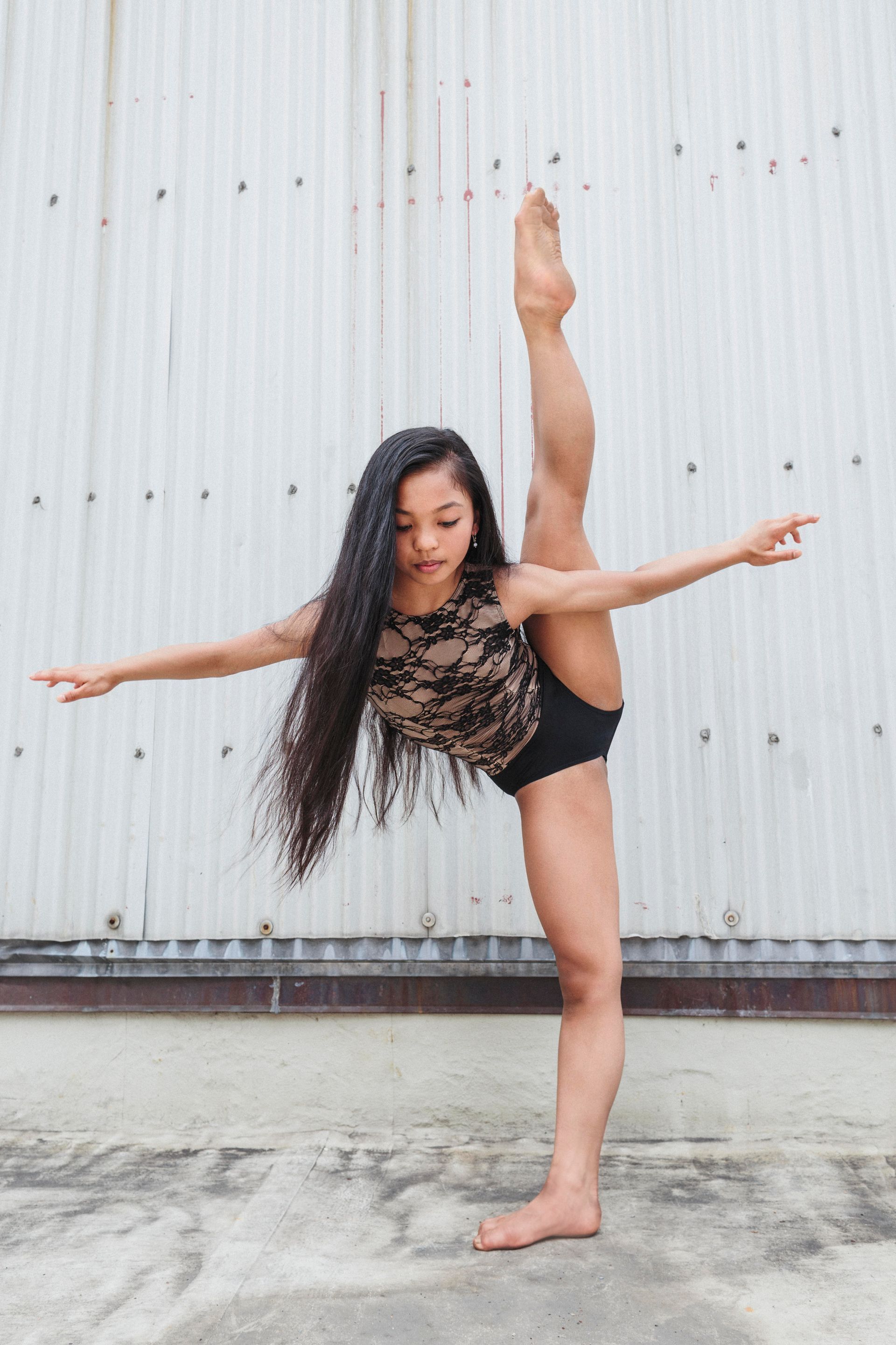 A young girl is doing a split in front of a white wall.
