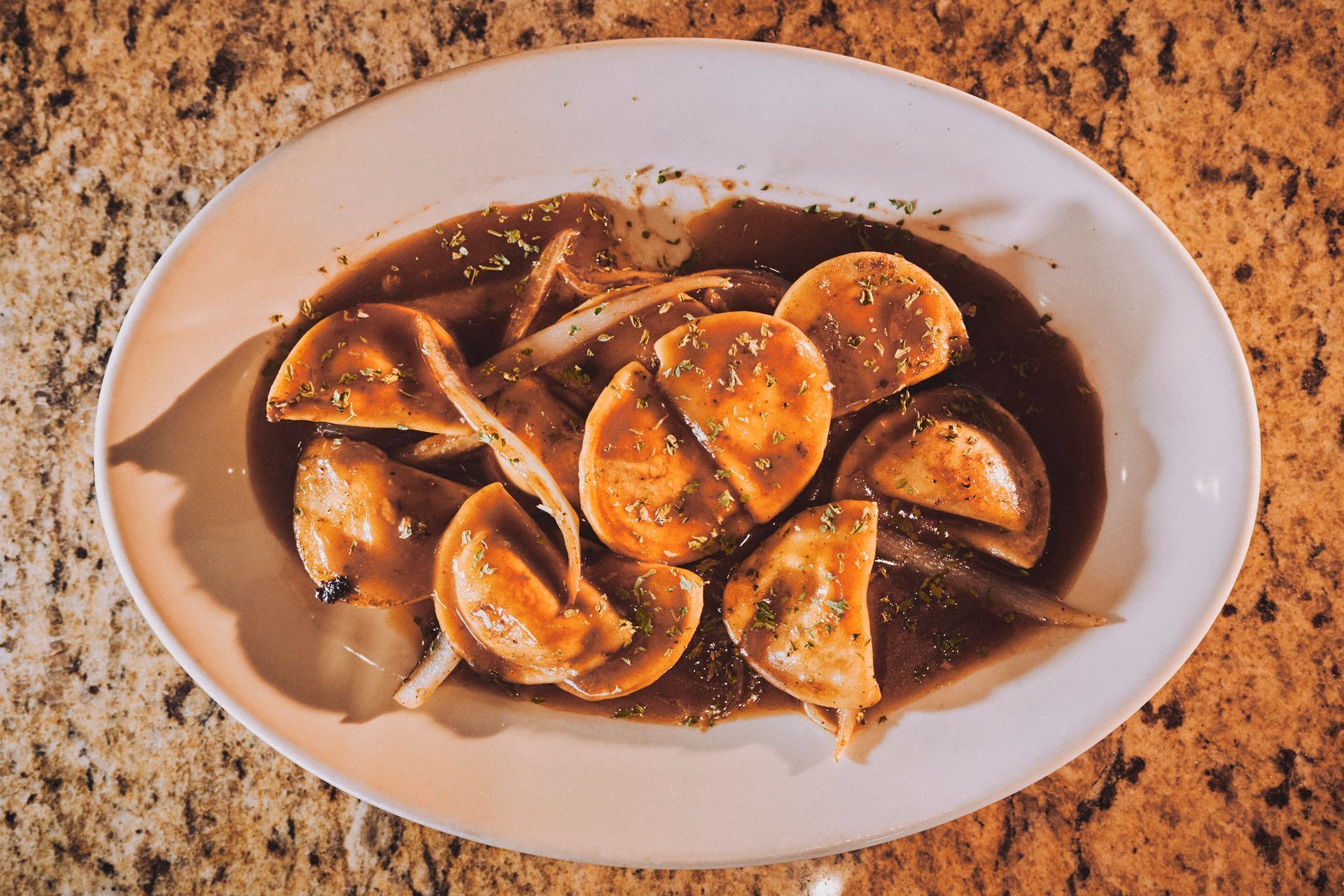 A white plate topped with ravioli and gravy on a table