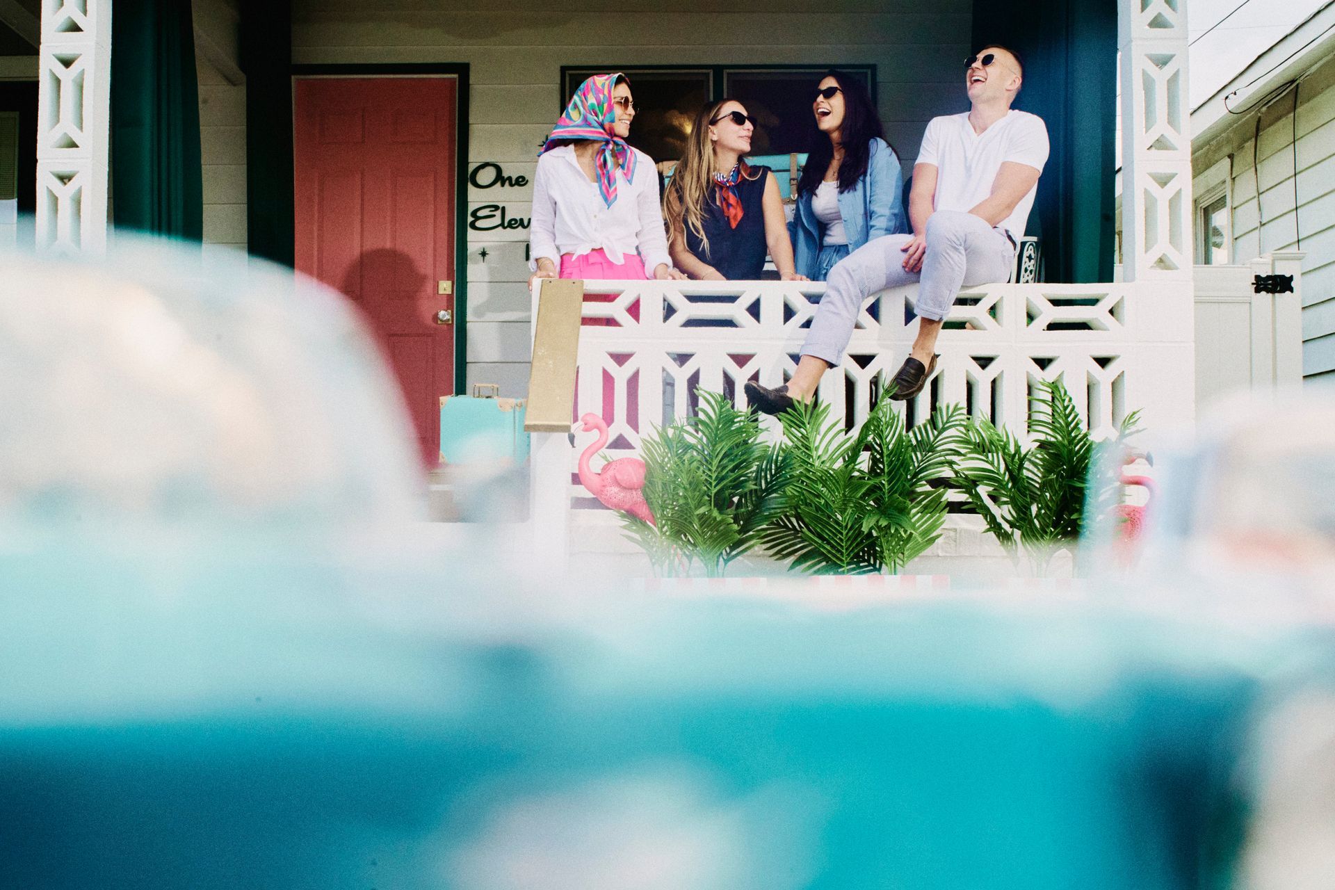 Woman in white dress and scarf on a rock by the sea, holding scarf above her head in sunlight.