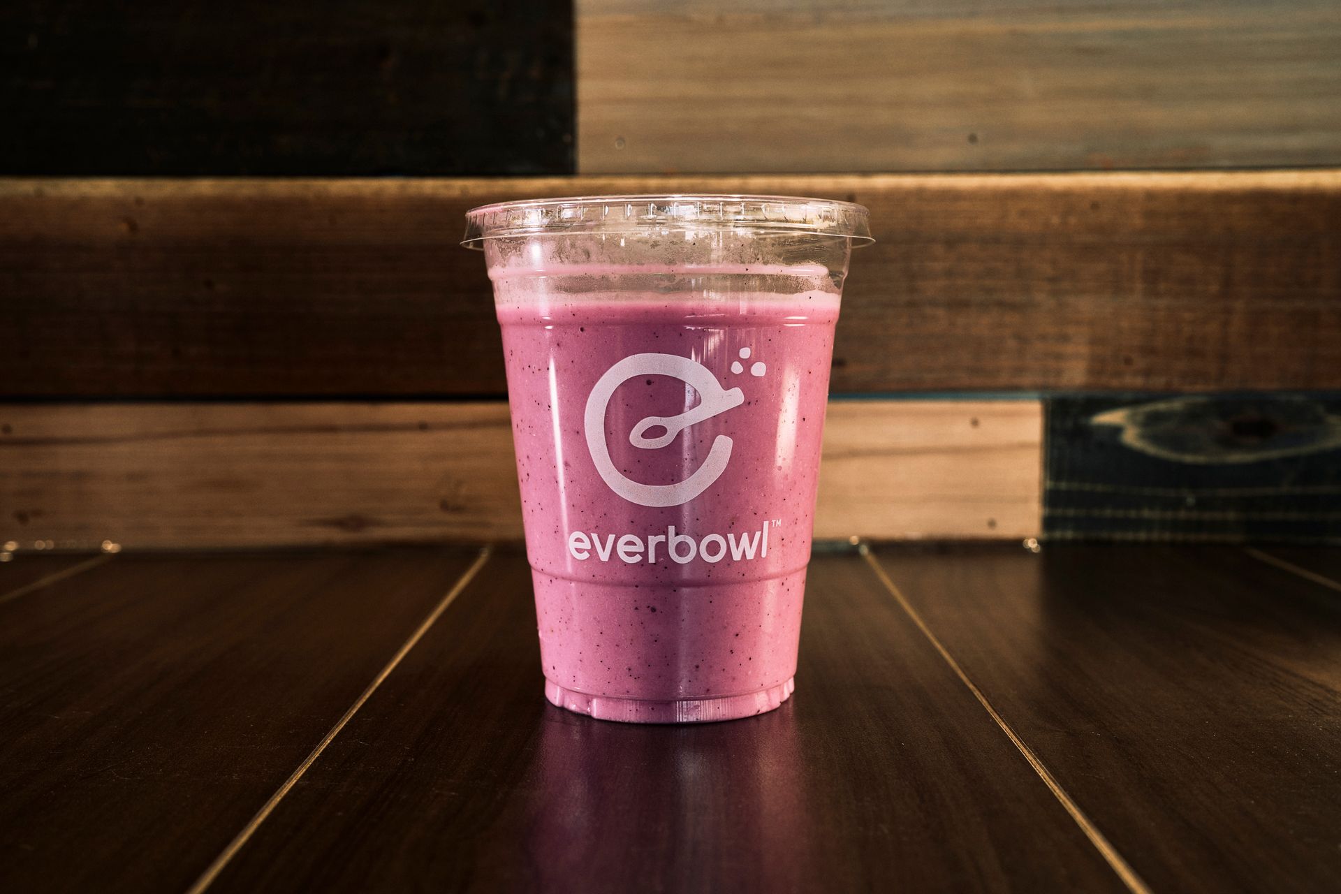 A smoothie in a clear cup with a logo on a wooden table.