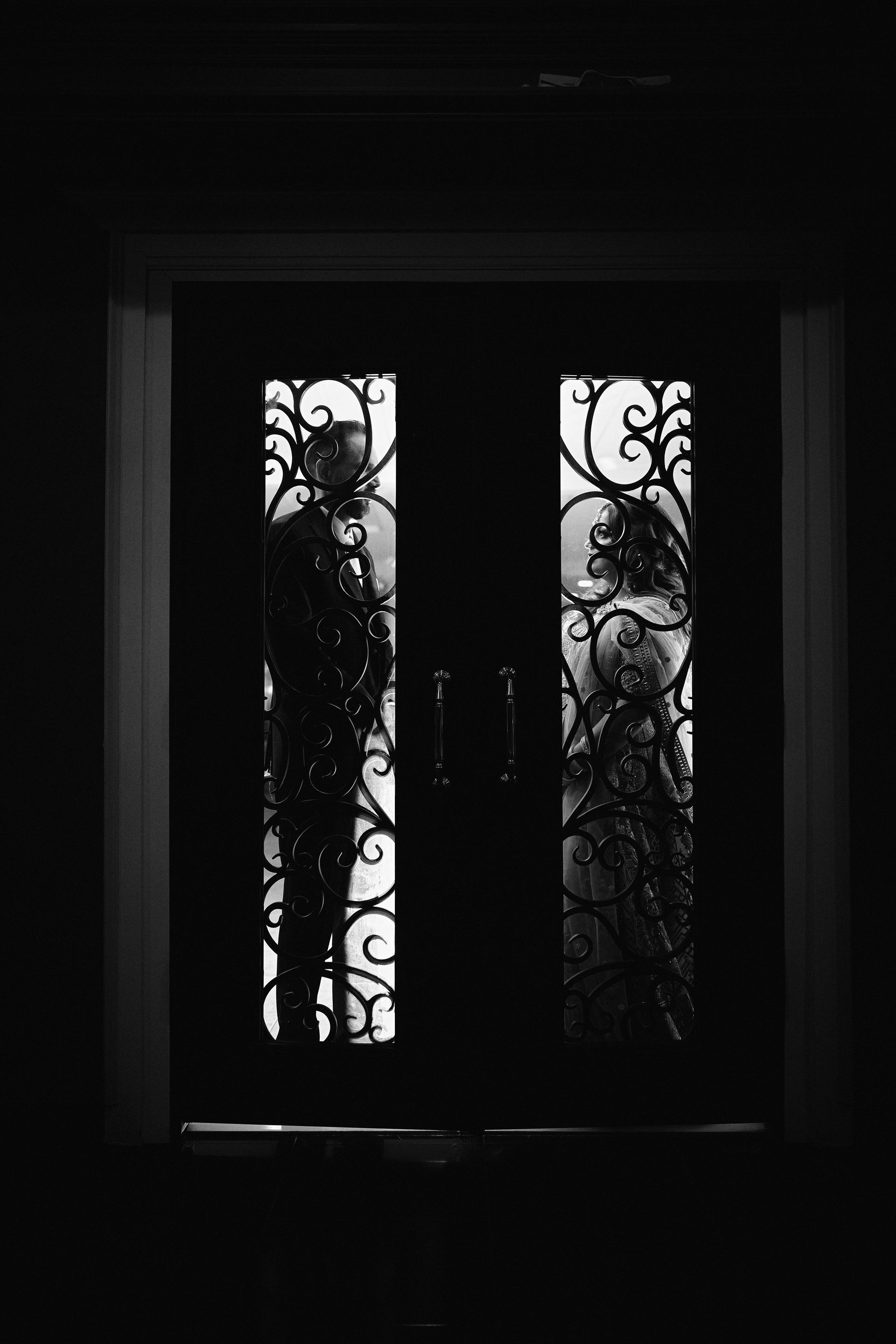 Black and white photo of silhouetted couple behind ornate doorway.