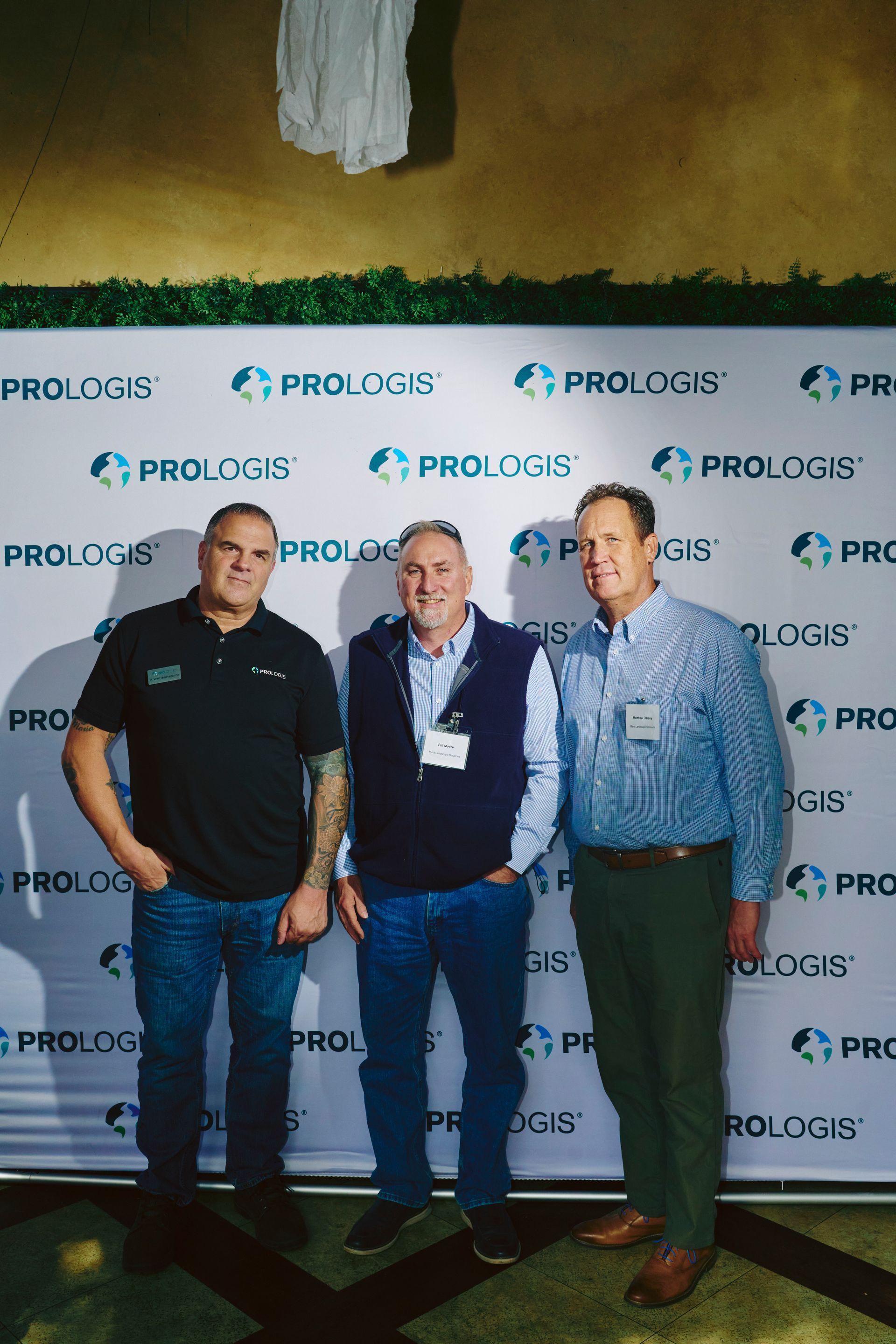 Three men posing in front of a backdrop with the company logo, Prologis.