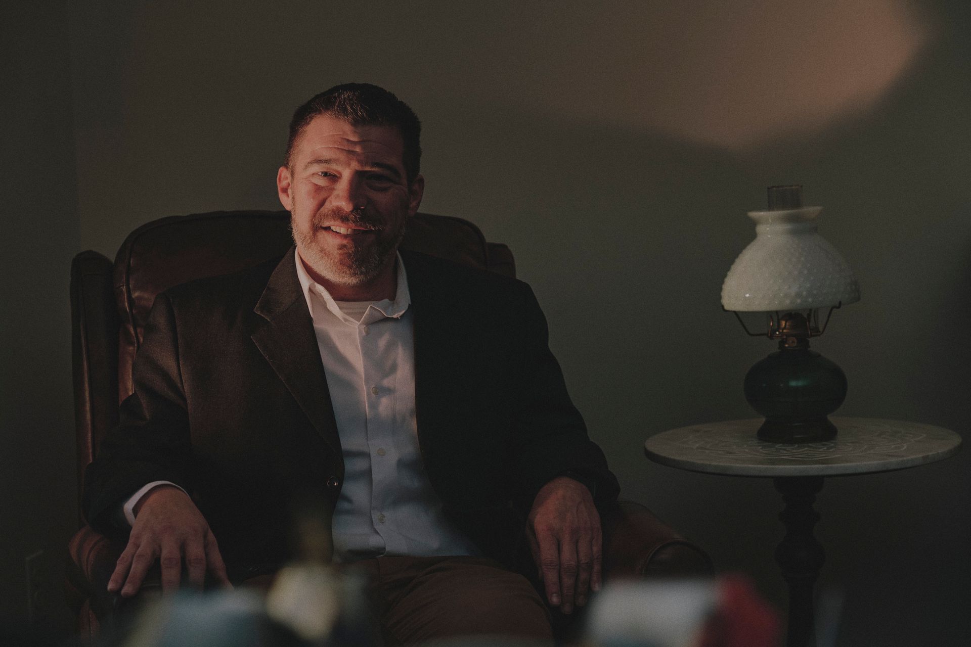 A man in a suit is sitting in a chair in front of a lamp.