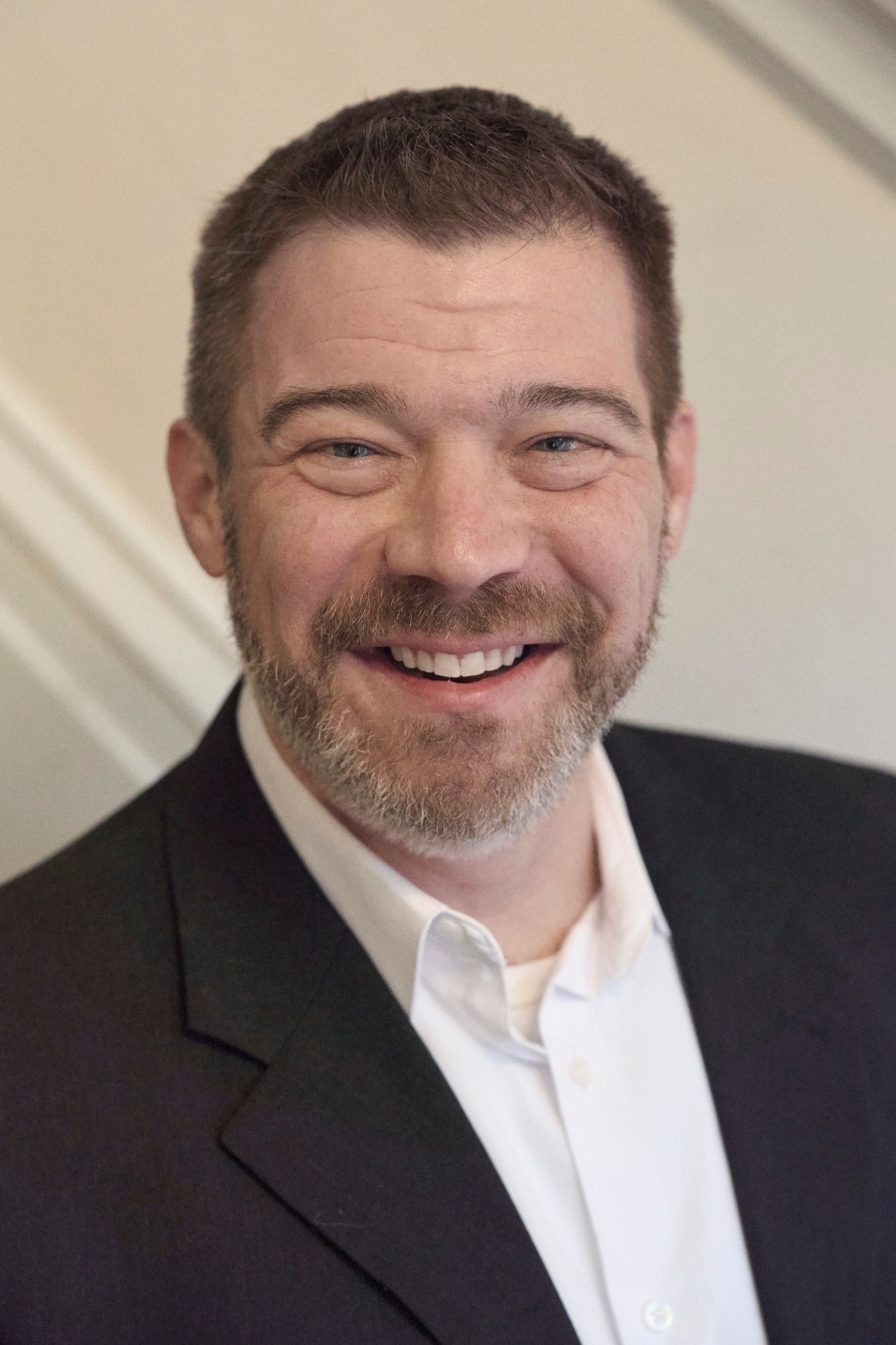 A man in a suit and white shirt is smiling for the camera.