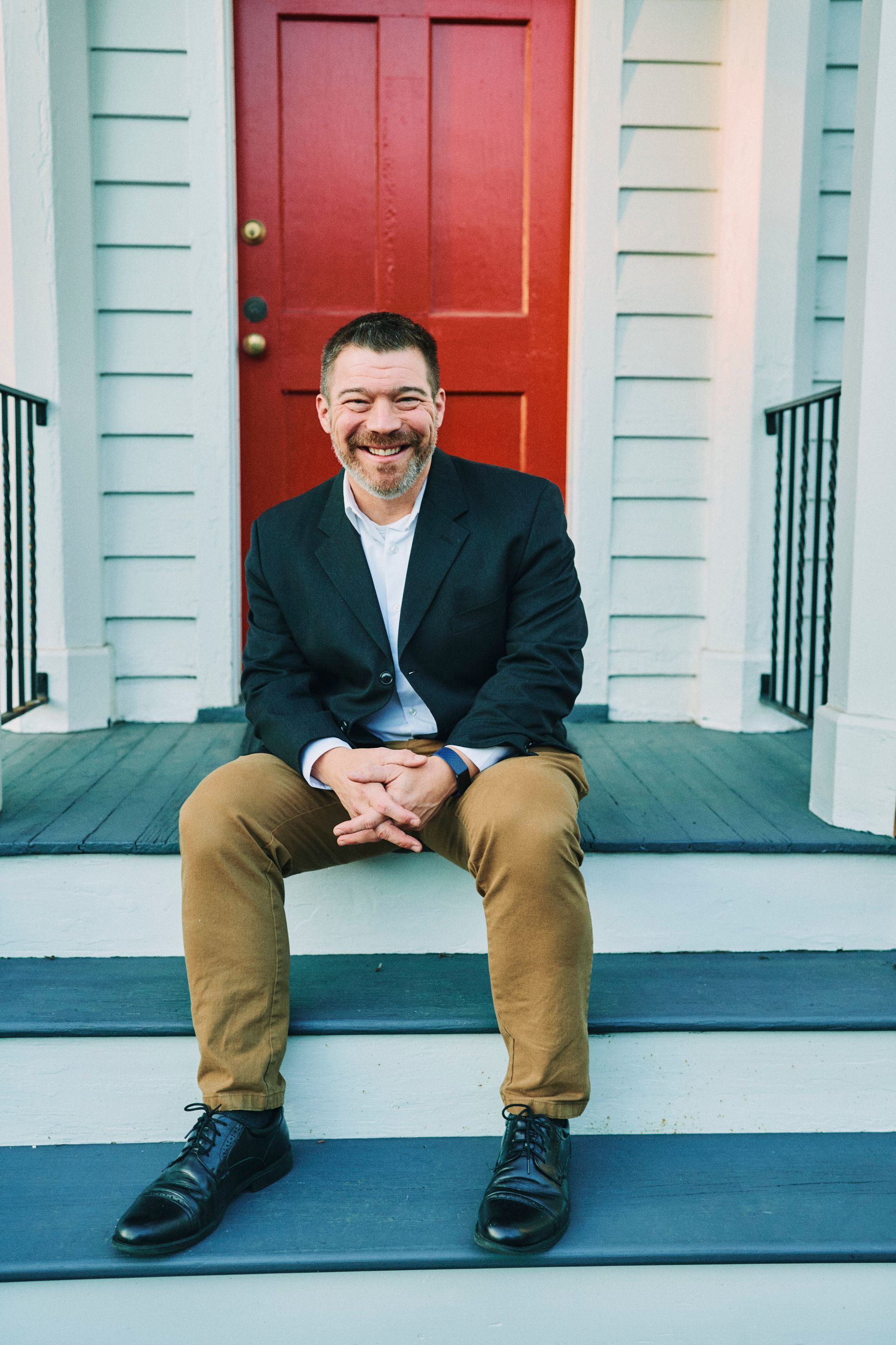 A man in a suit is sitting on the steps of a house in front of a red door.