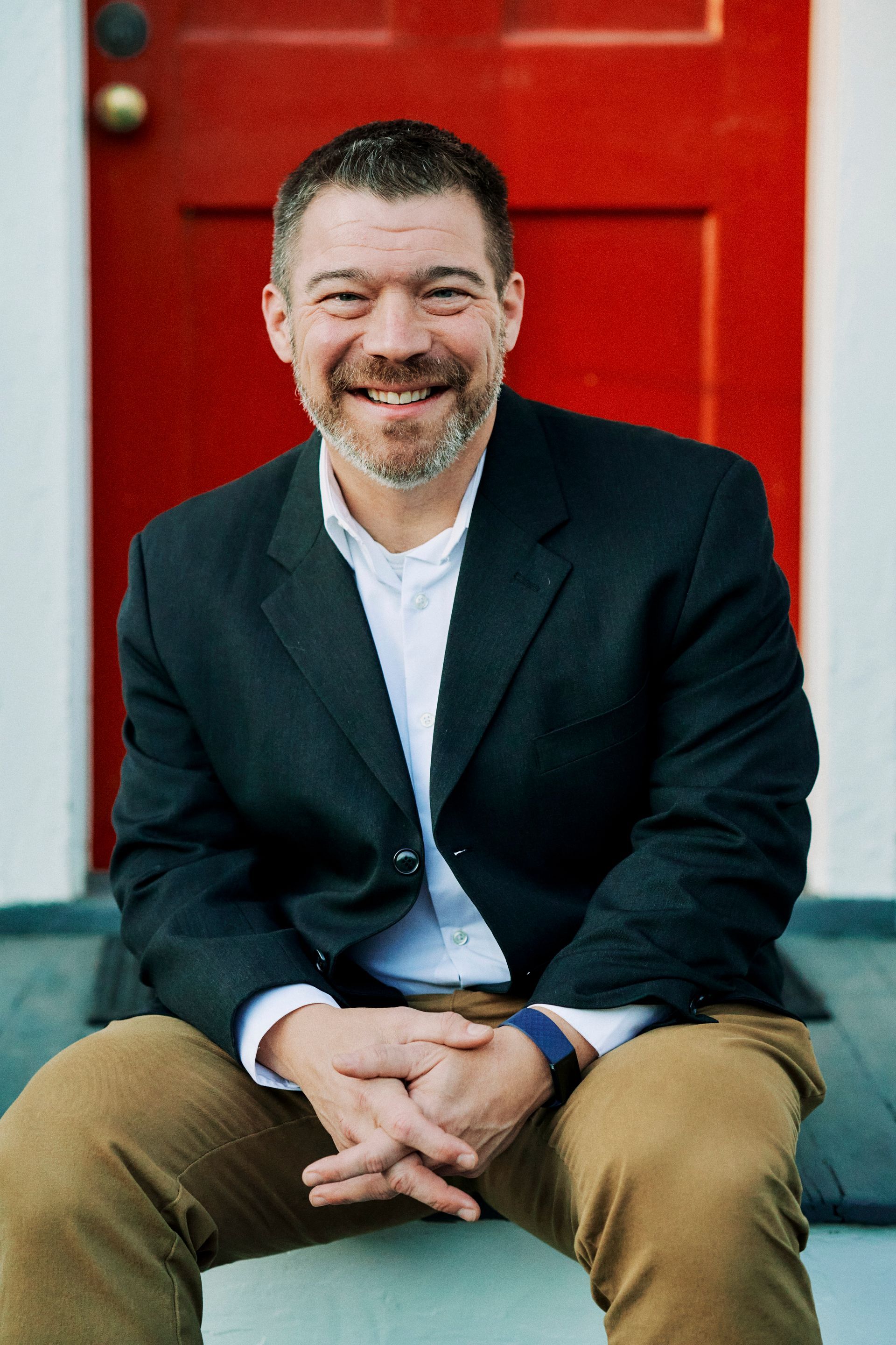 A man in a suit is sitting in front of a red door.