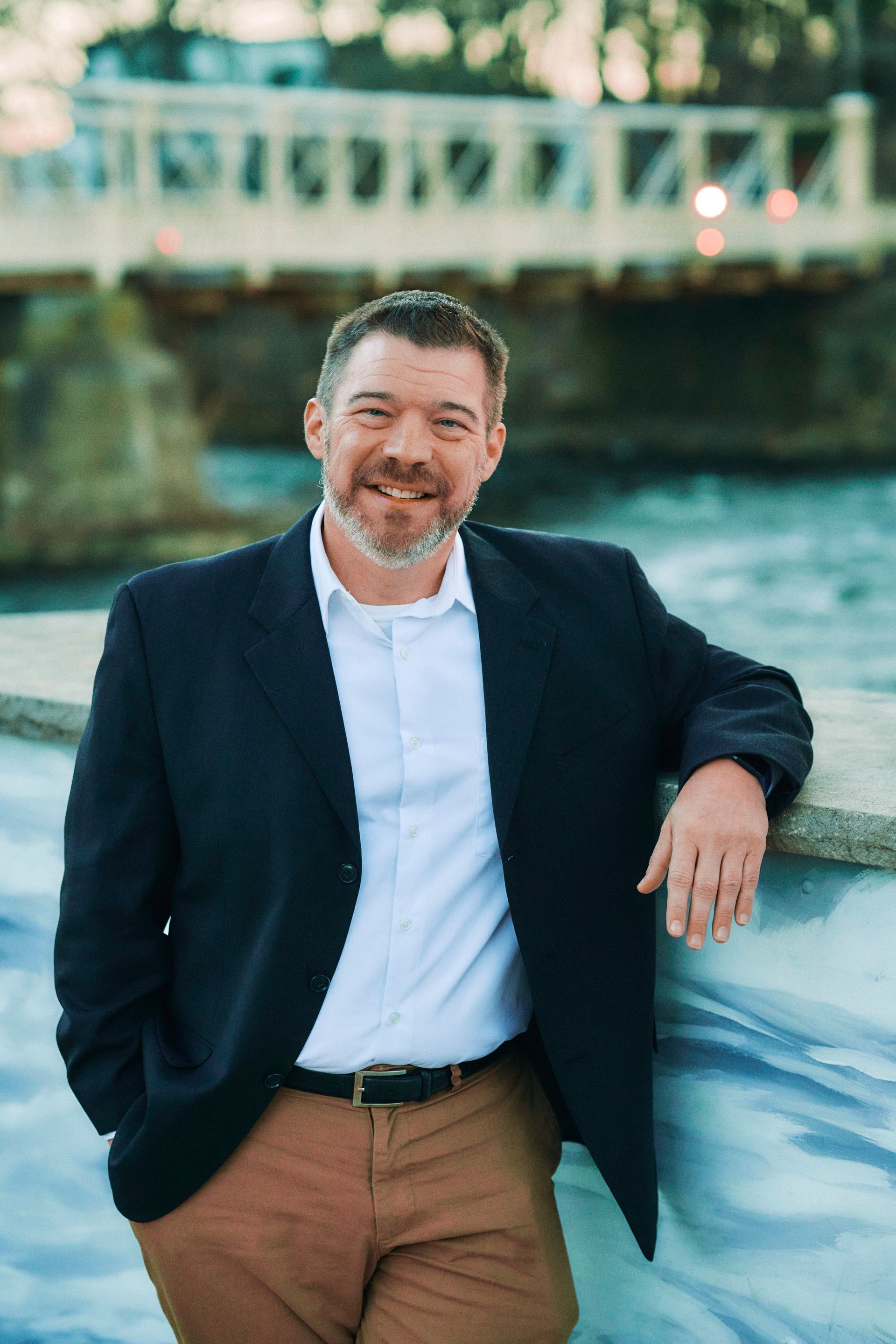 A man in a suit is leaning against a wall next to a river.