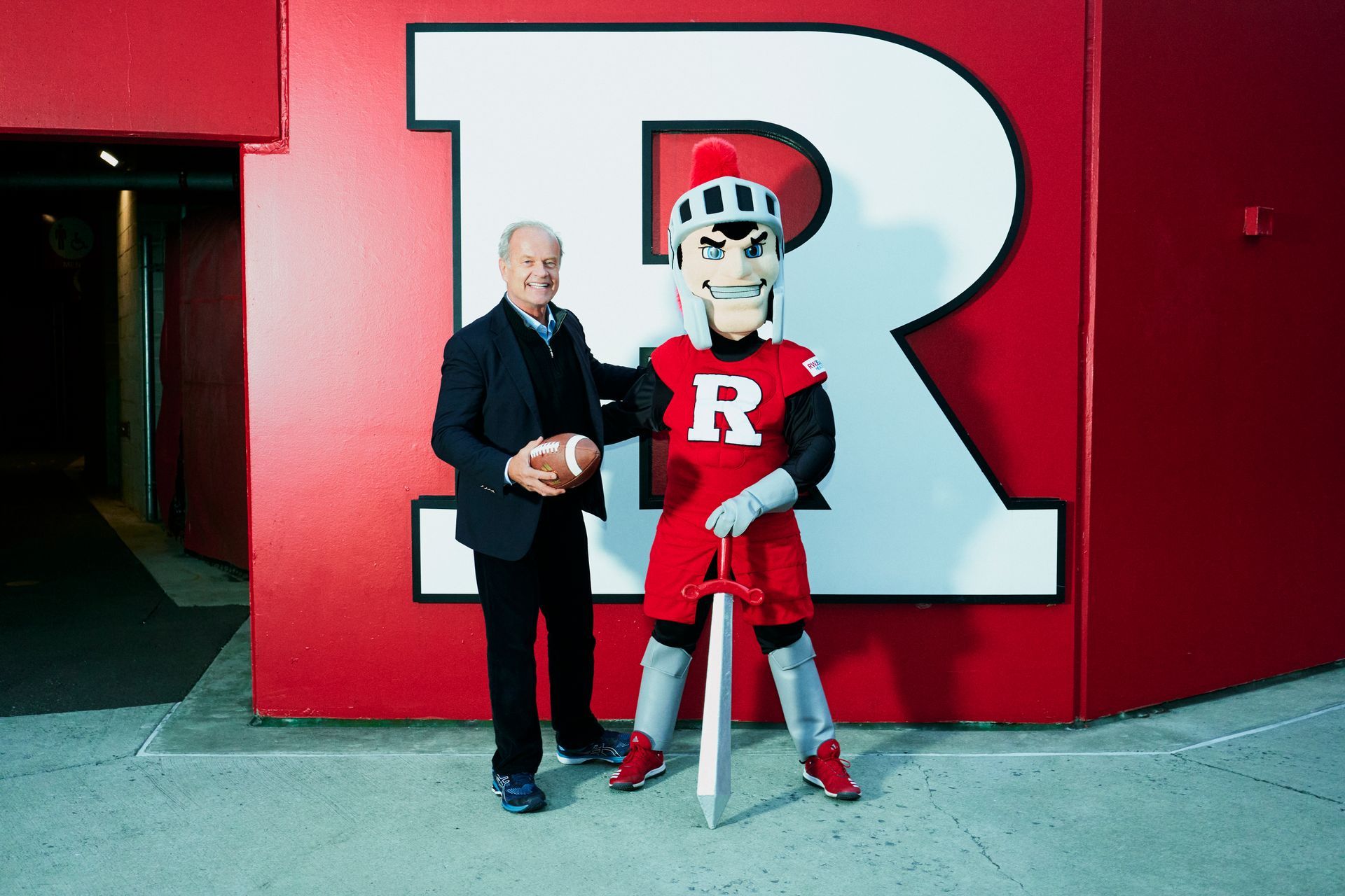 Man with football and Rutgers mascot in front of a large red