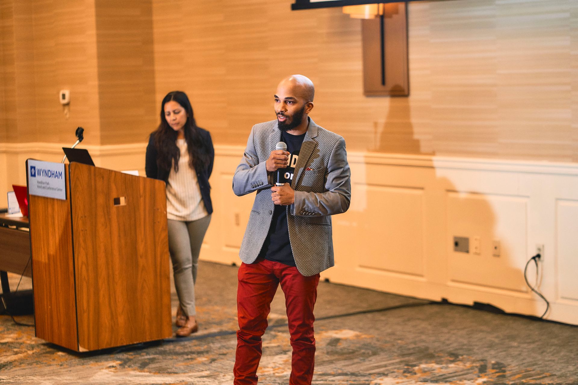 Man speaking at podium with woman standing behind; formal event setting.