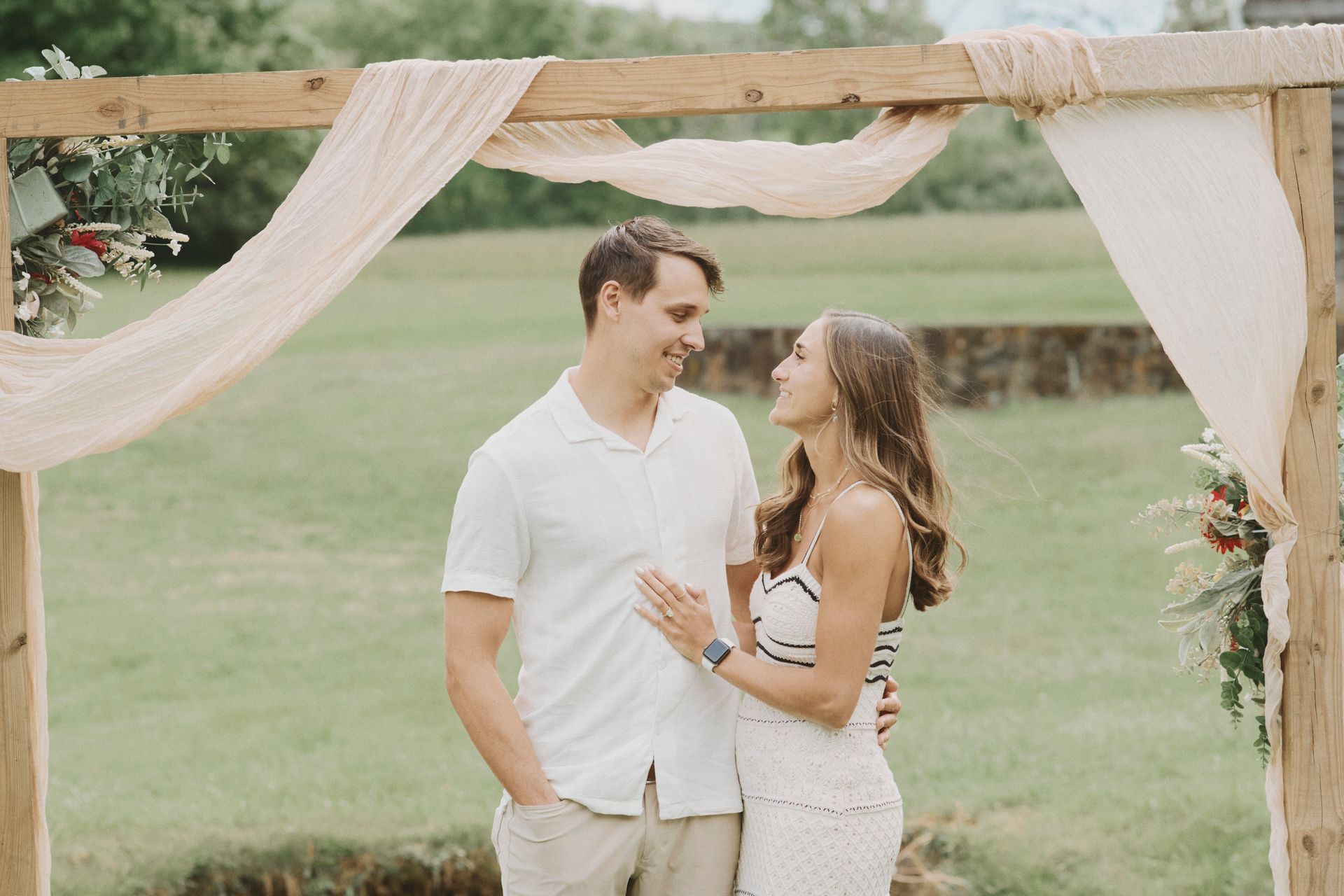 A man and a woman are standing under a wooden arch in a field.