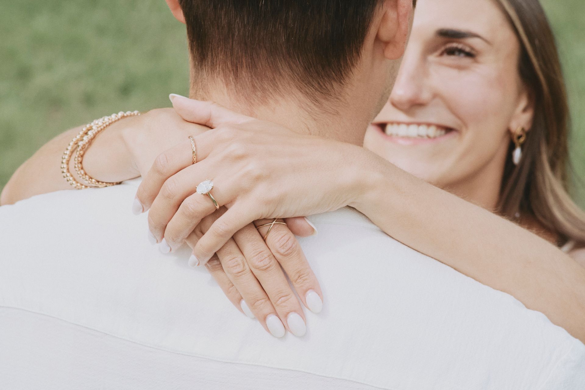 A woman is hugging a man with an engagement ring on her finger.