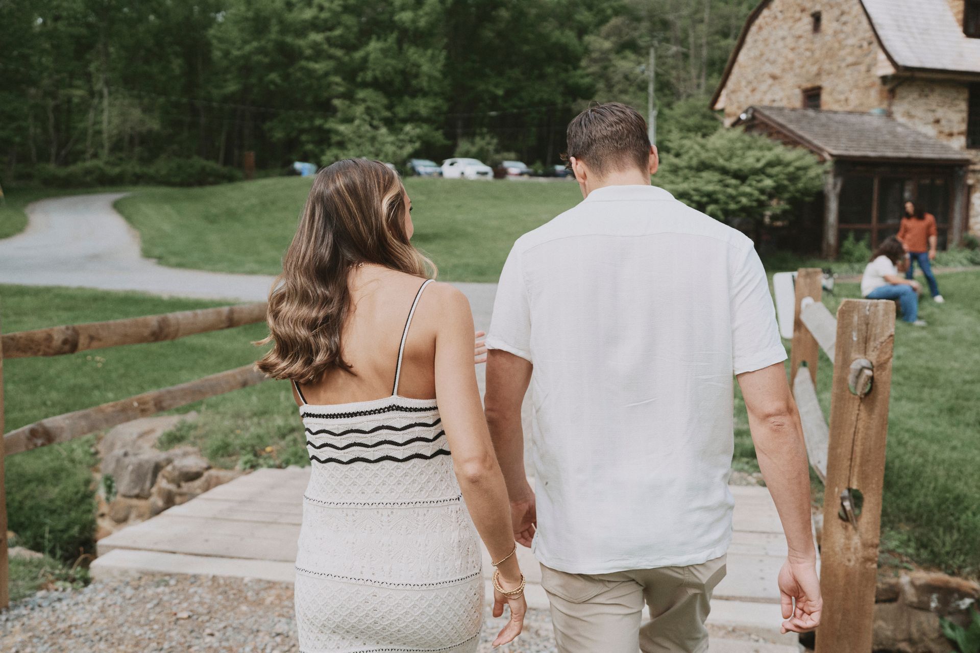 A man and a woman are walking across a bridge holding hands.