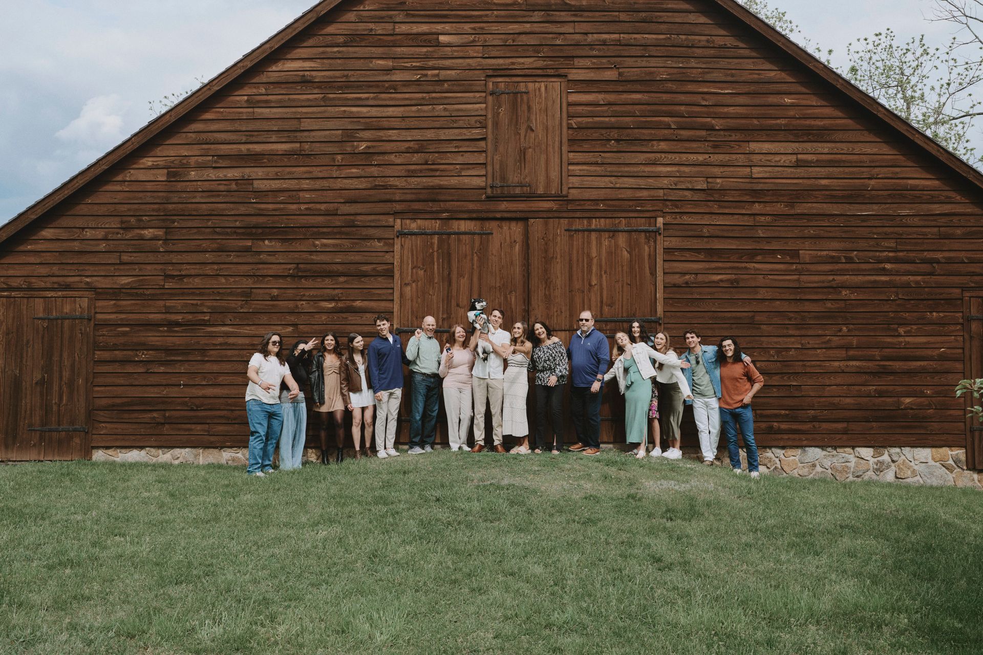 A large group of people are standing in front of a wooden barn.
