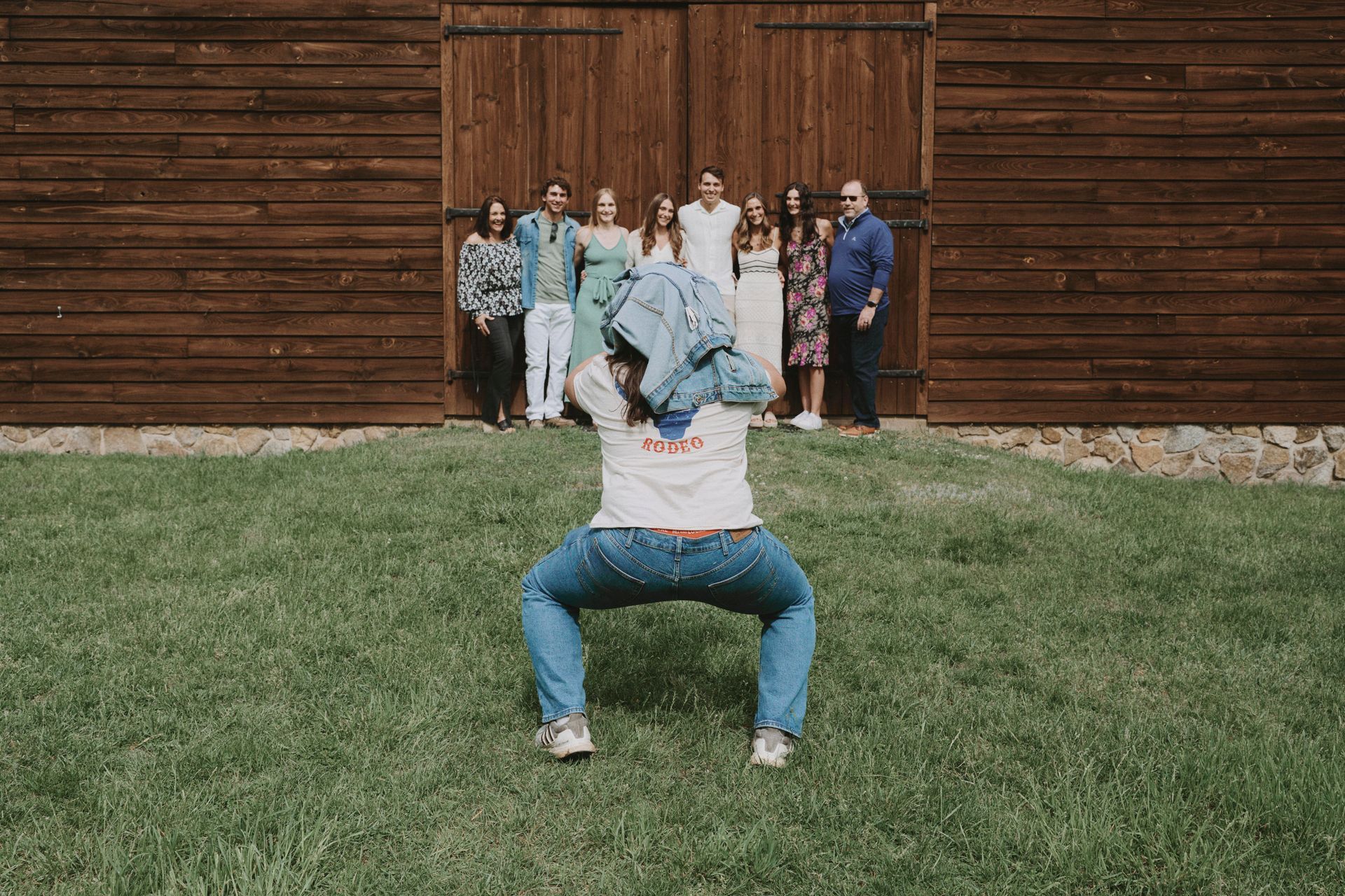 A man is squatting in front of a group of people standing in front of a barn.