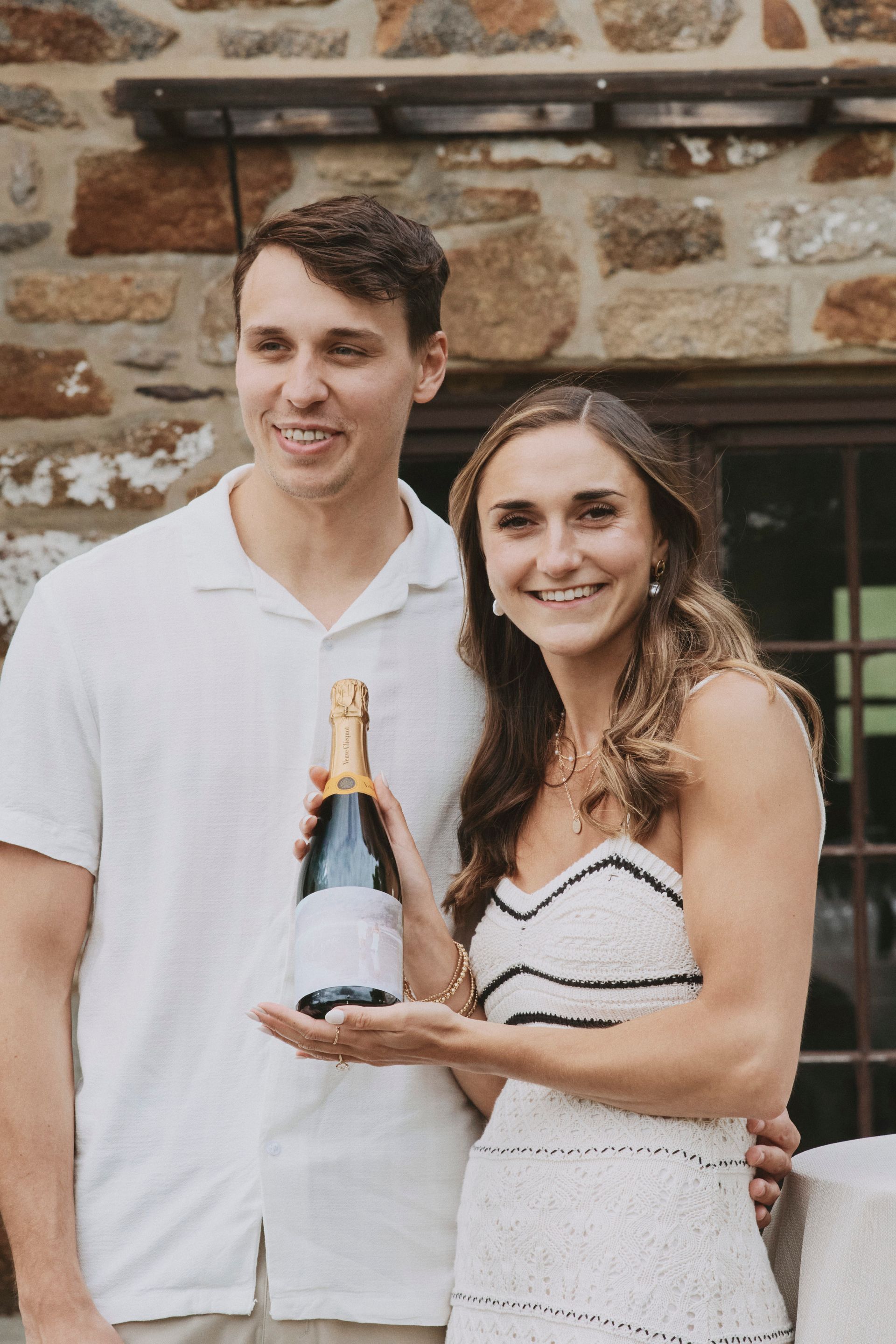 A man and a woman are standing next to each other holding a bottle of champagne.