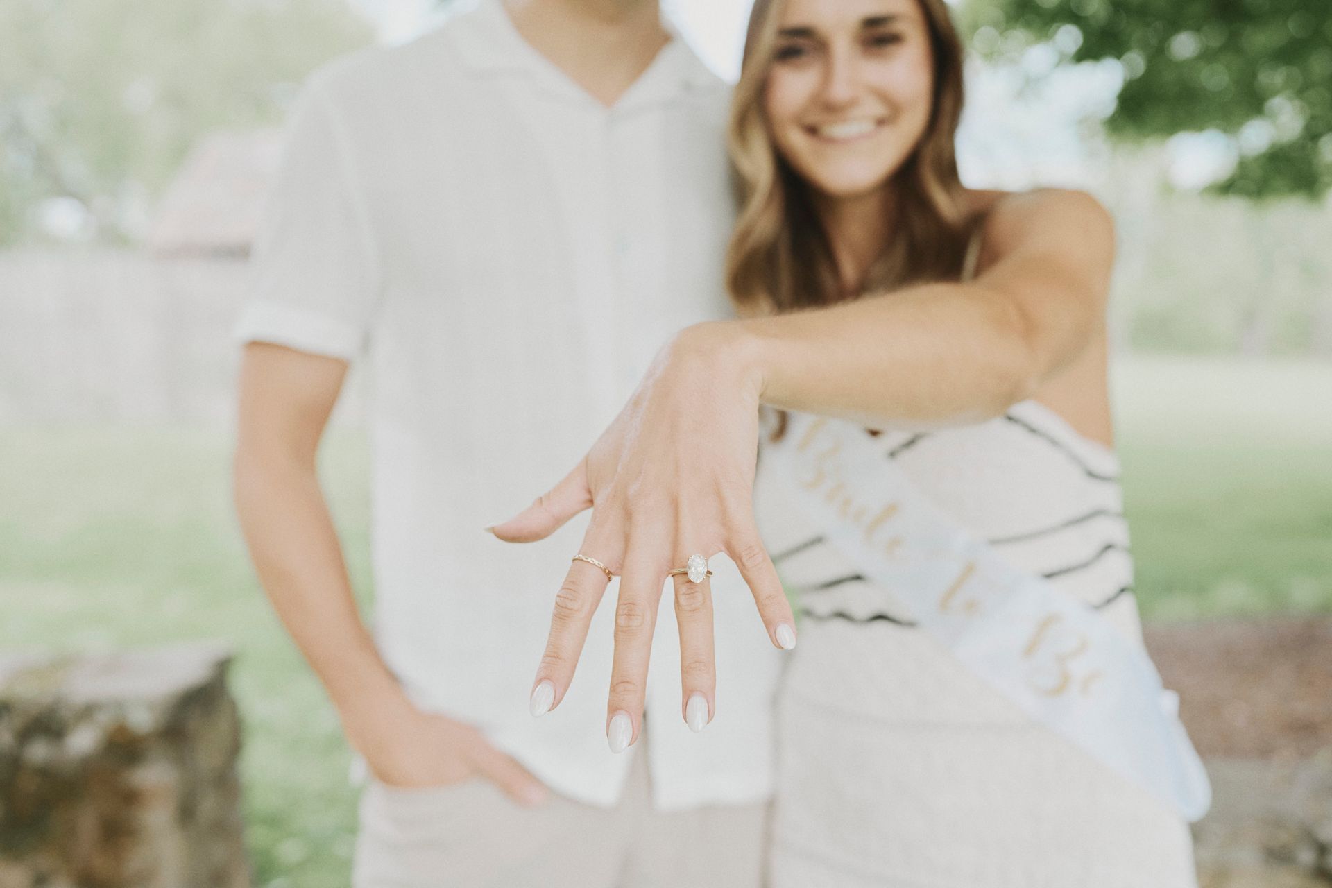 A man and a woman are standing next to each other and the woman is showing off her engagement ring.