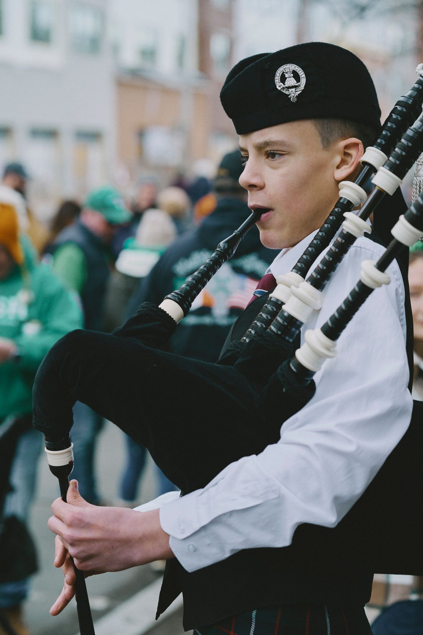 A young man in a white shirt and black beret playing bagpipes at a parade.