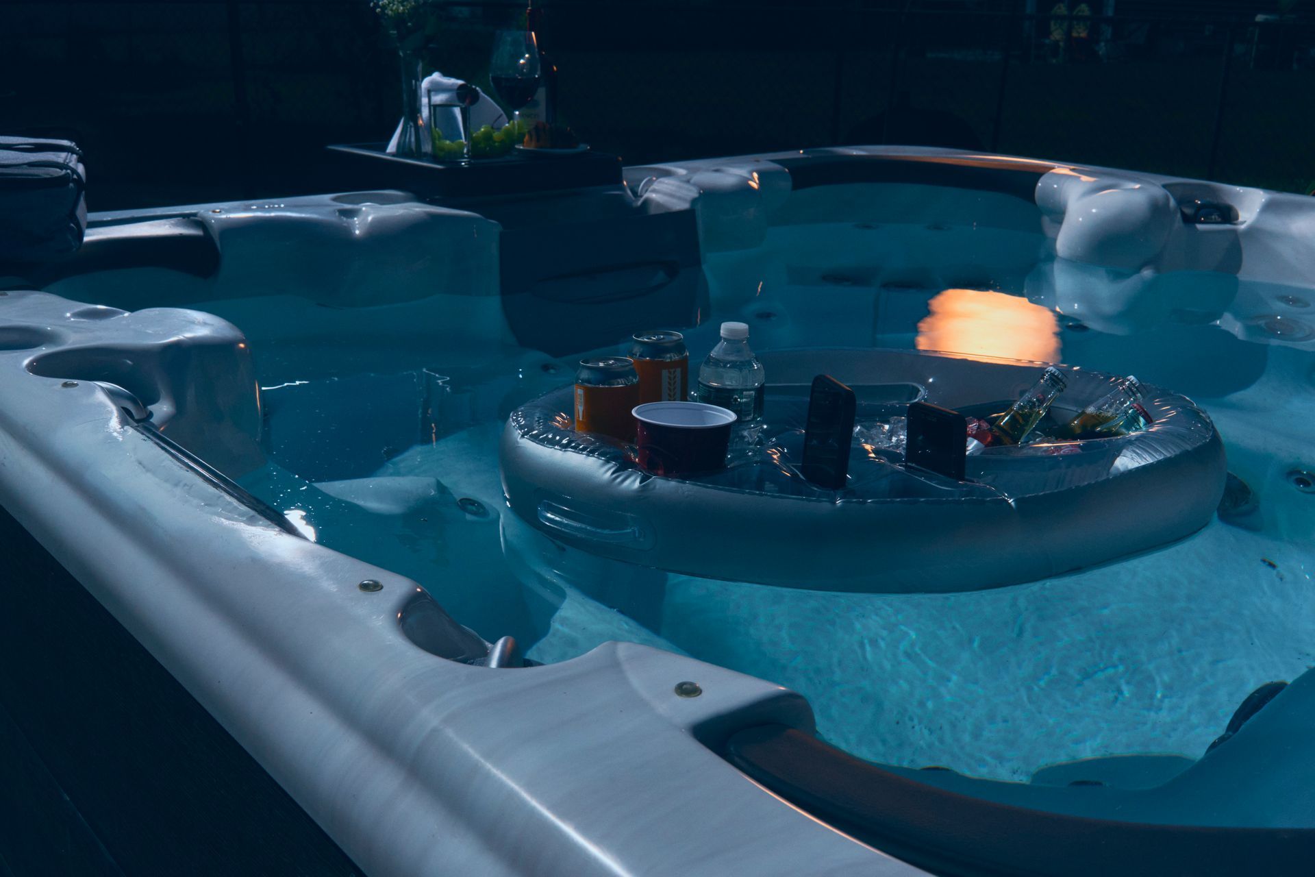 Hot tub at night with a floating tray holding drinks and a lit candle.