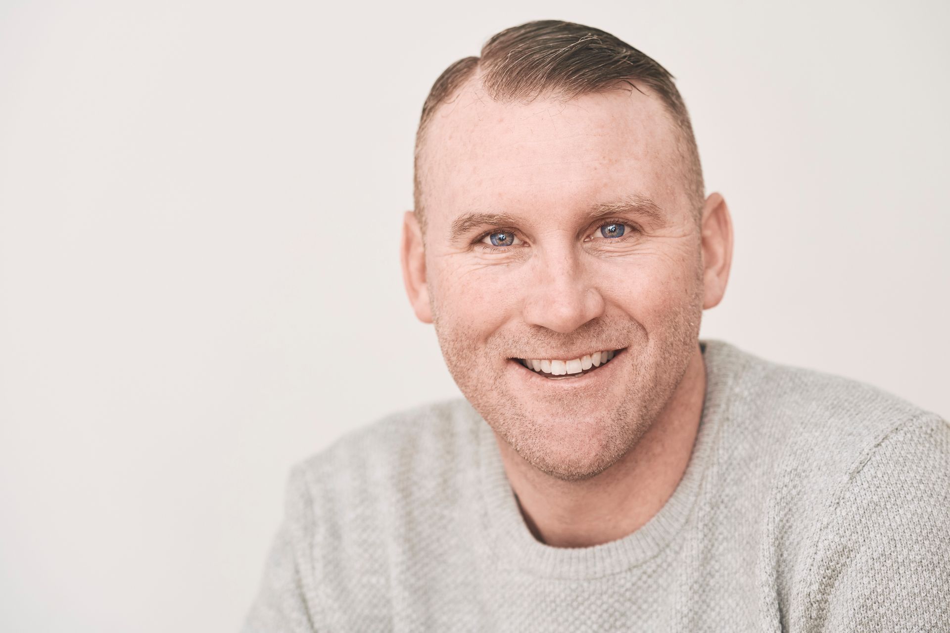 Smiling man with fair skin and buzzed hair wearing a gray sweater.