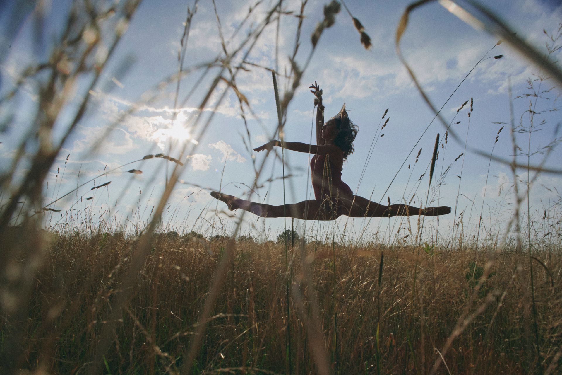 A woman is jumping in the air in a field of tall grass.