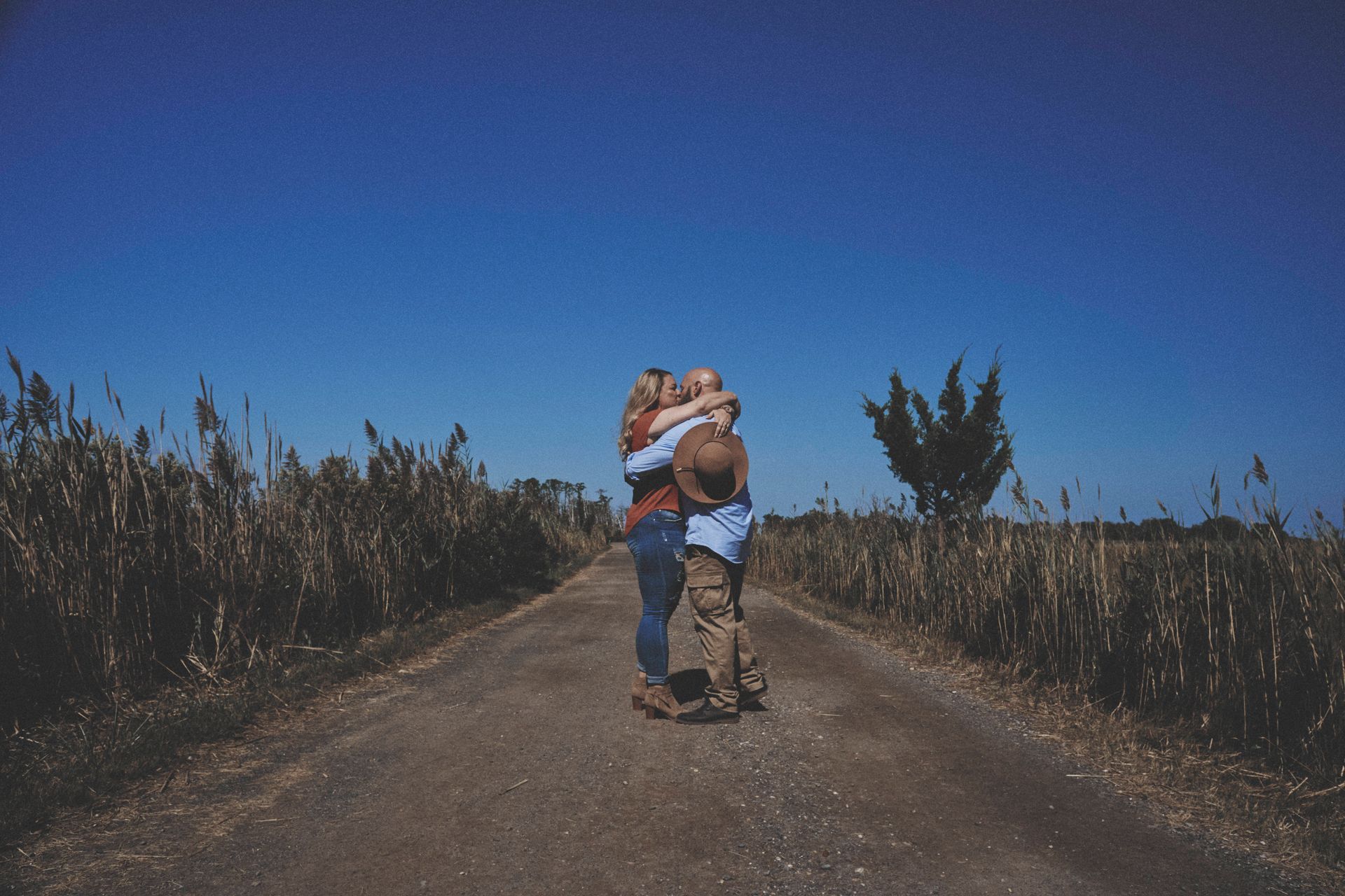 Family embraces on a dirt road, surrounded by tall grass under a blue sky.
