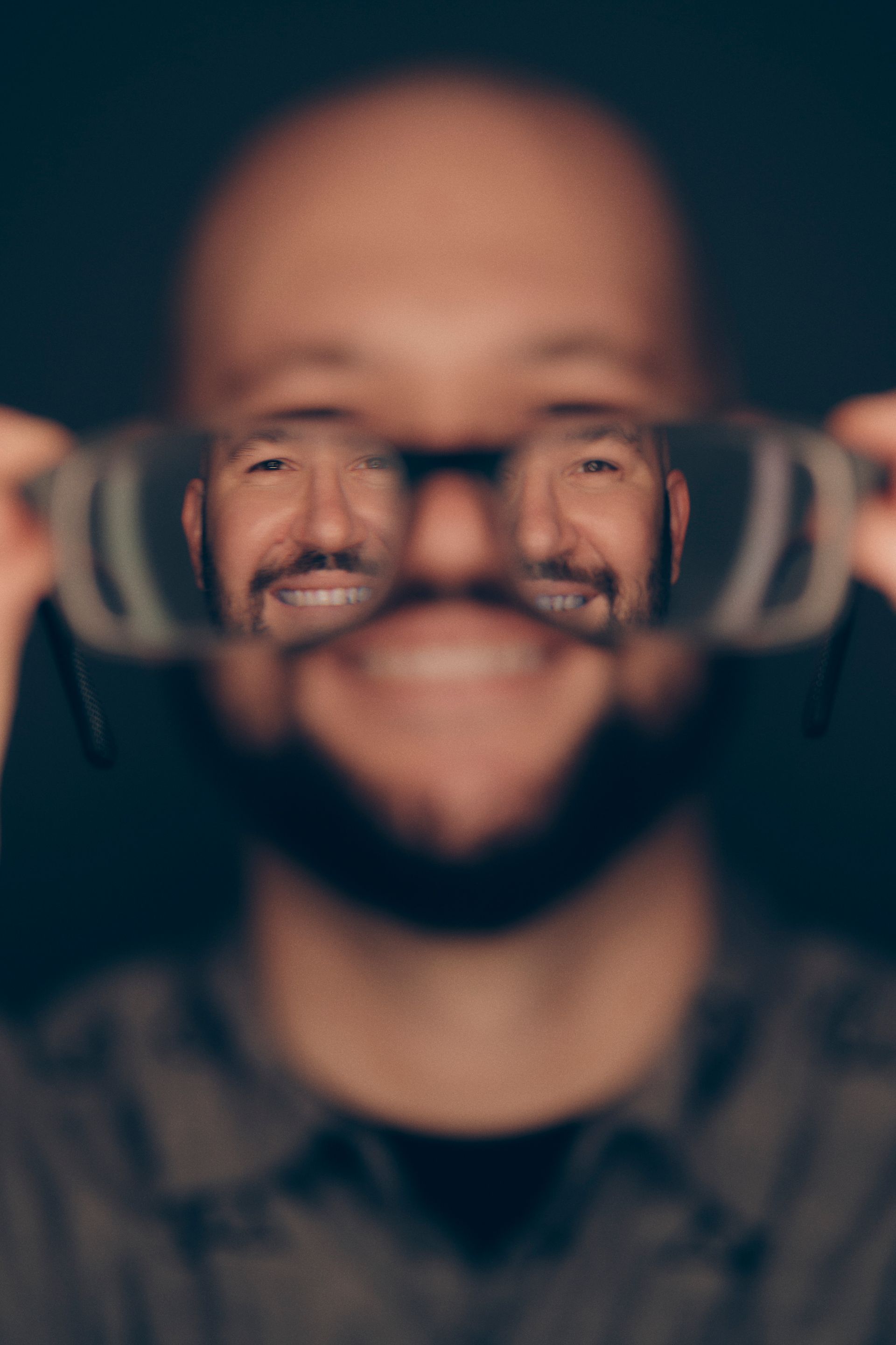 A man with a beard is holding a pair of glasses in front of his face.